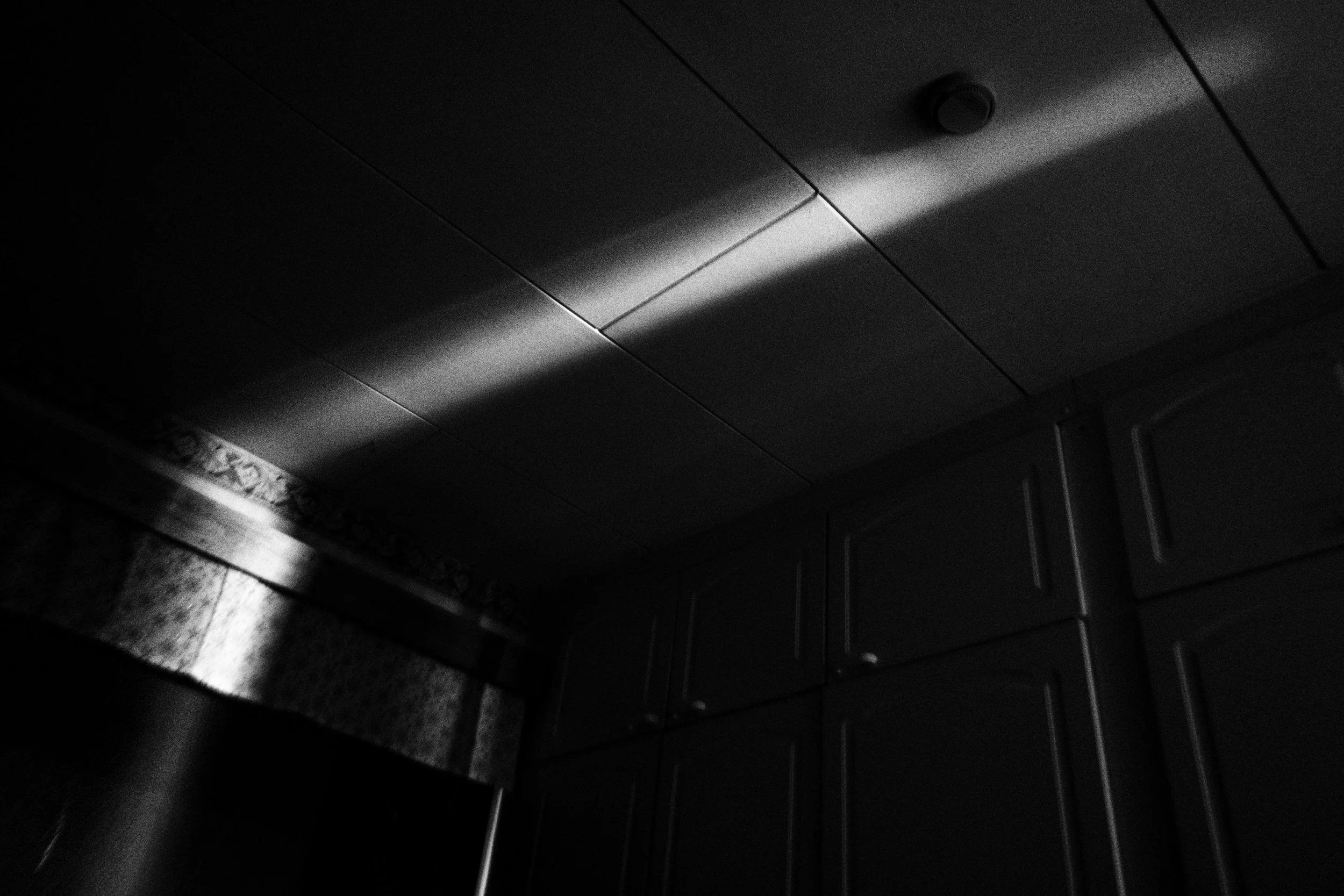 A black-and-white high contrast photograph showing a ray of light against the ceiling of a dark bedroom.