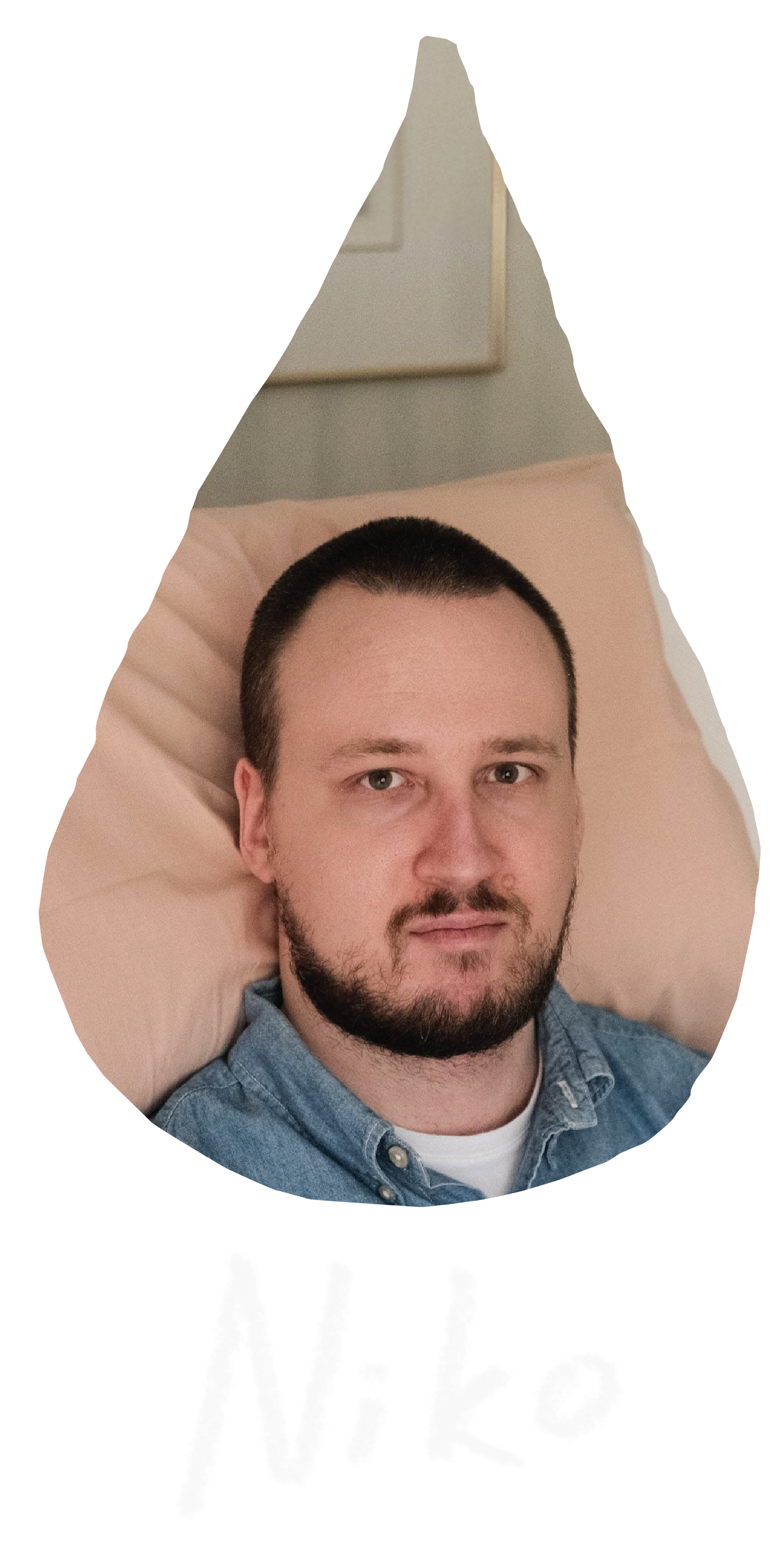 A raindrop shaped image of Niko, a white man with short dark hair and a beard sits upright in a hospital bed with a neutral expression. He is wearing a denim button-up shirt and a gold watch on his wrist. The setting is a bedroom.