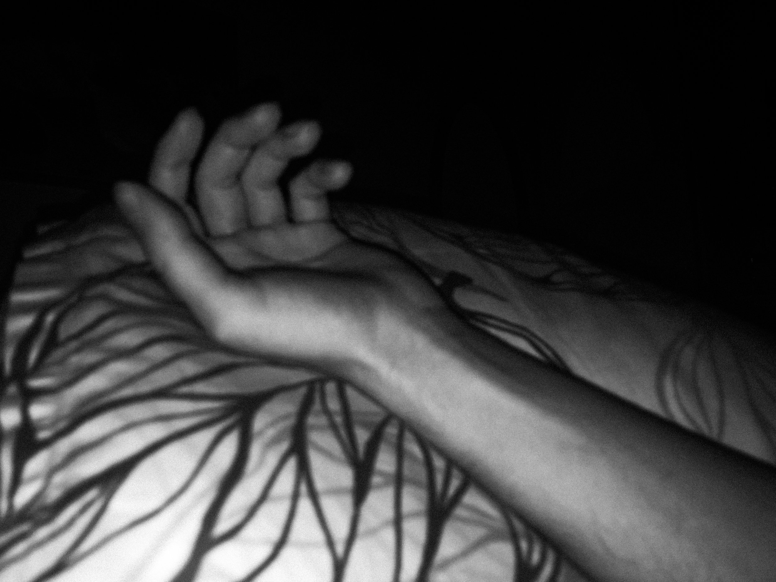 A black-and-white photo of a hand resting on a pillow, lit by a flash in an otherwise dark bedroom.