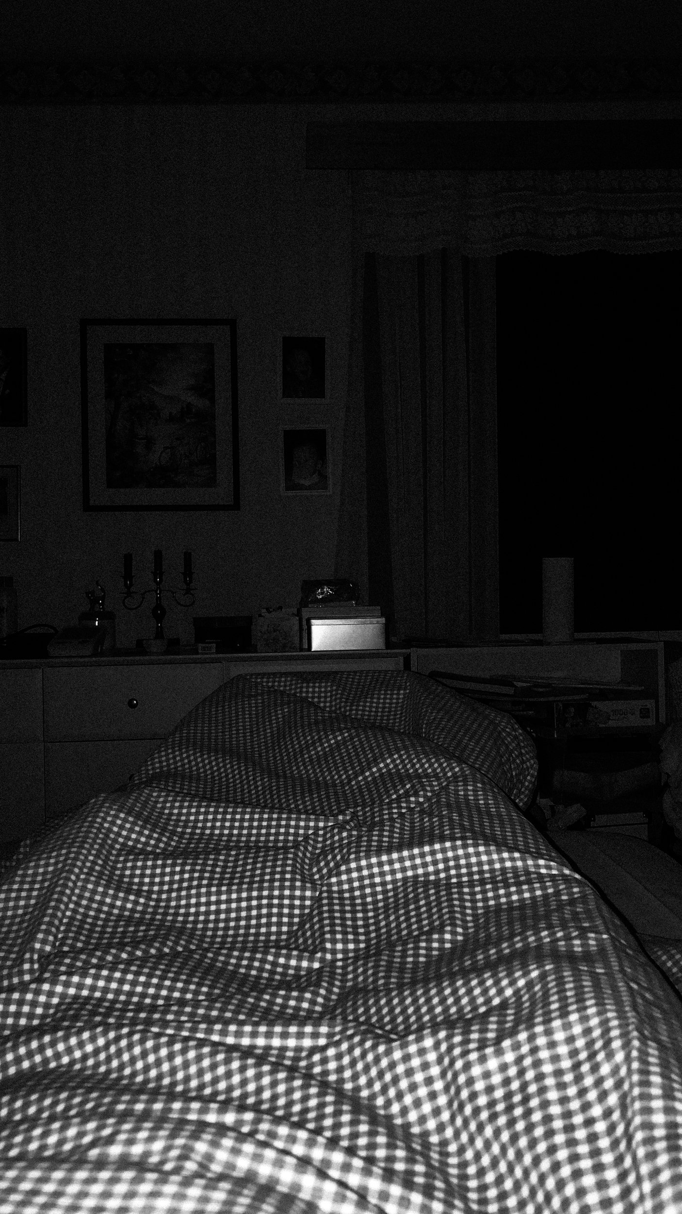 A black-and-white photo taken from Niko’s point of view that shows his pitch-black bedroom; the flash of the phone camera lights parts of his blanket.