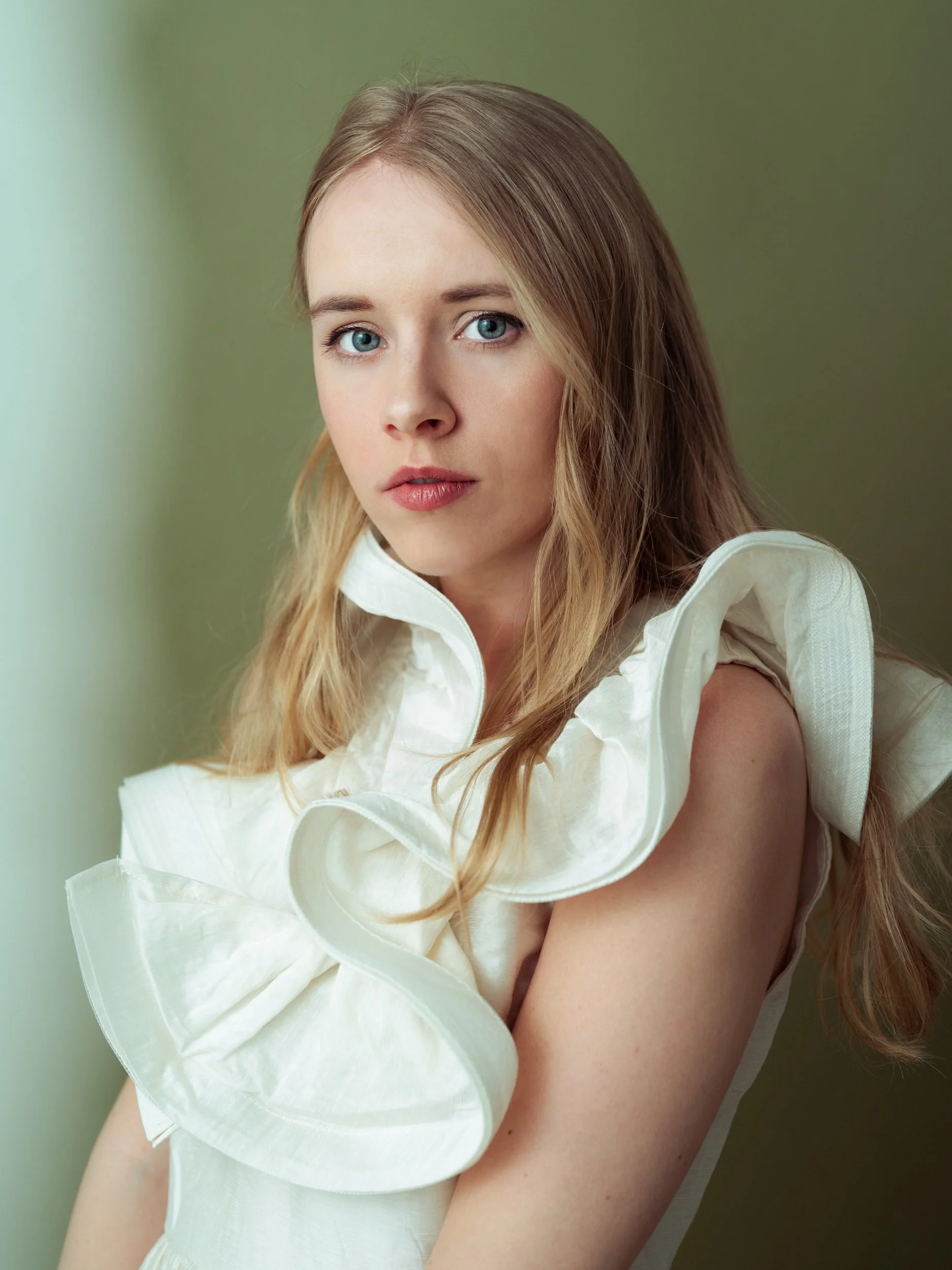 Mirthe, a white woman with blonde hair and blue eyes, wearing a white blouse, looking at the camera.