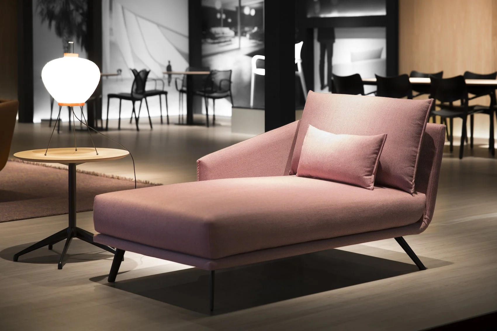 Sofá moderno rosa con cojín en un espacio interior con lámpara y área de comedor al fondo.