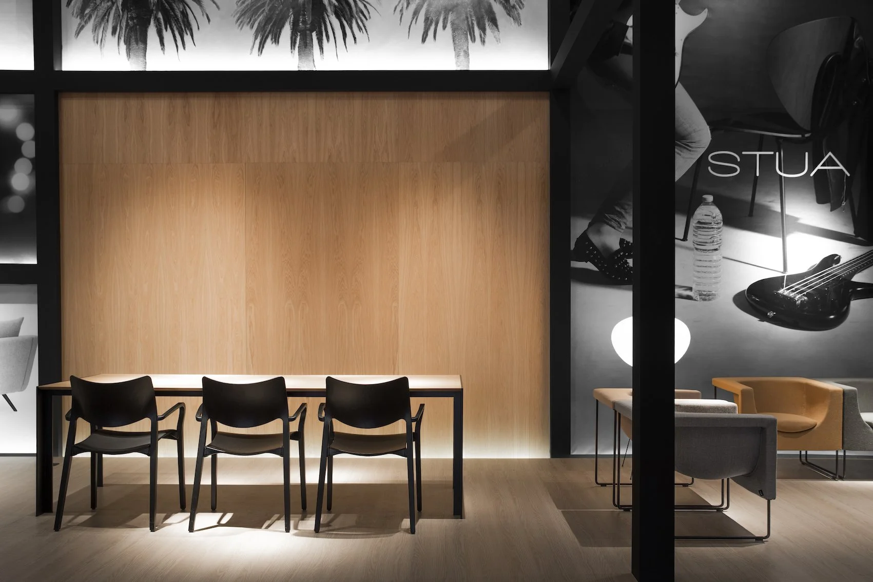 Interior de un espacio moderno con muro de madera y muebles negros y beige, con cartel que dice 'STUA' y posters en la pared con imágenes en escala de gris.