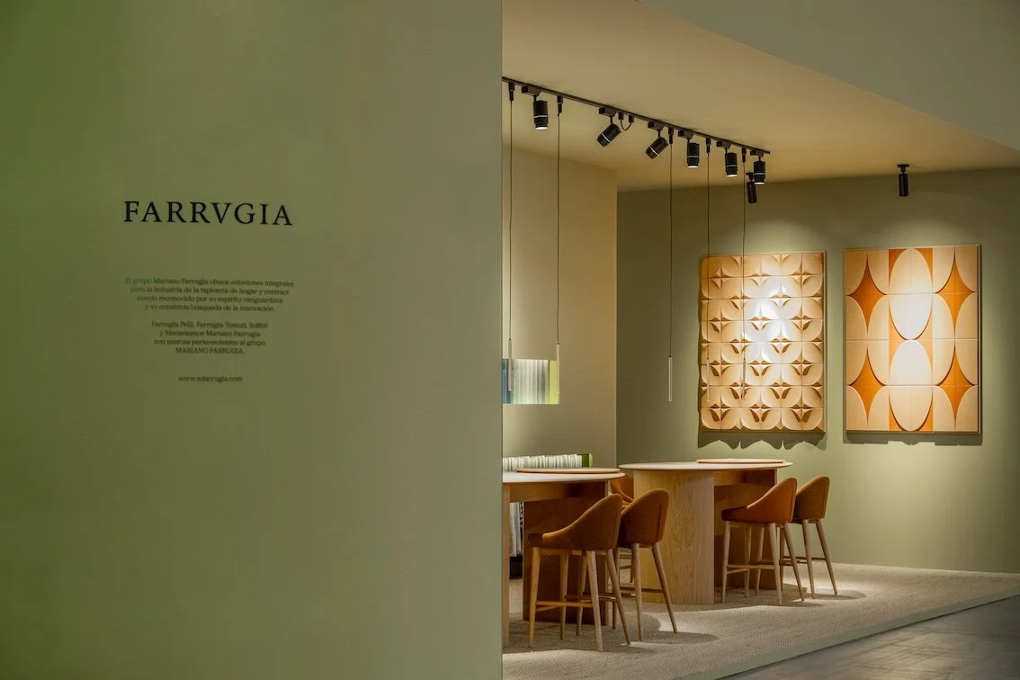 Sala de exposición con arte en la pared, lámparas de techo y sillones de madera con cojines en tonos naranjas.