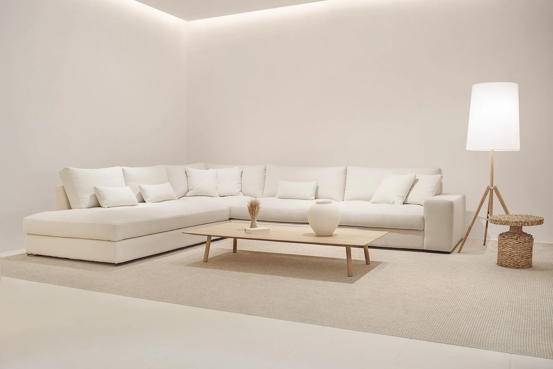 Sala de estar con sofá blanco y cojines, mesa de madera con objetos decorativos, lámpara de pie y alfombra beige en un ambiente minimalista.
