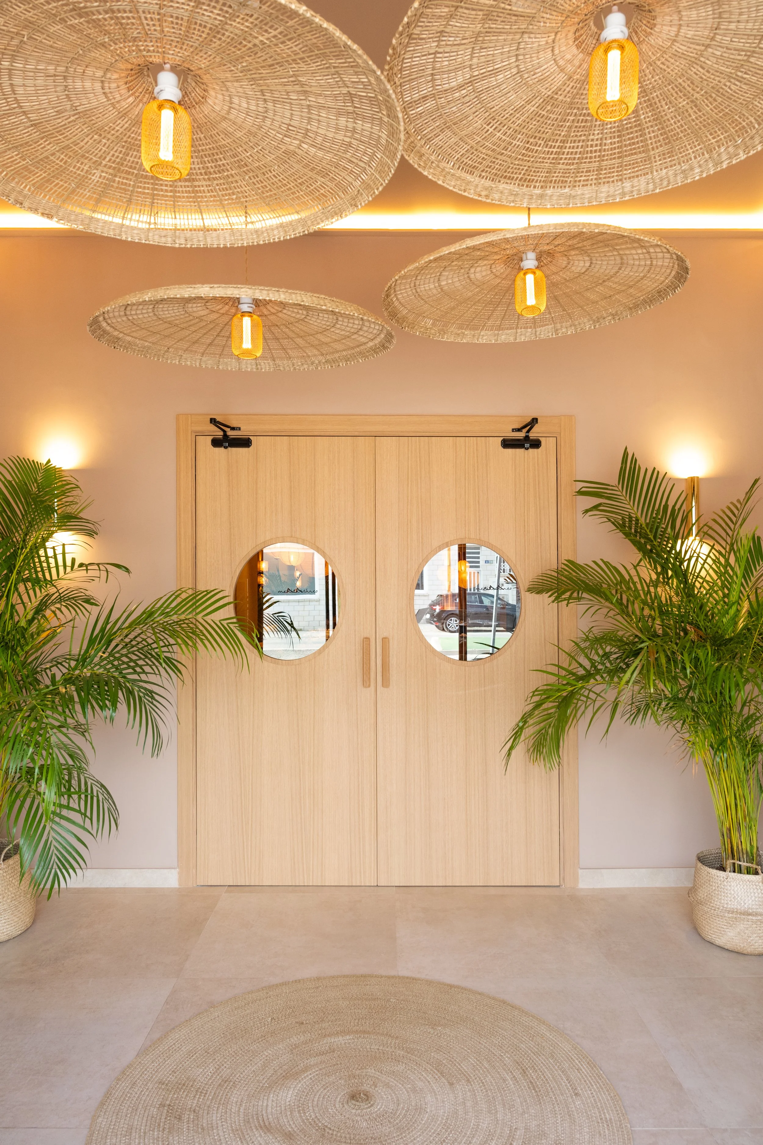 Puertas de madera con espejos redondos, plantas en cestos y lámparas de mimbre en el techo en un espacio interior bien iluminado.