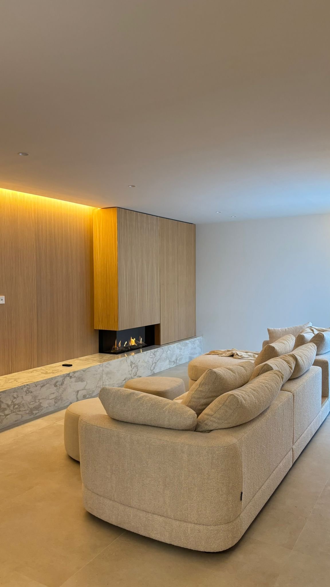 Sofás beige en una sala moderna con chimenea y pared de madera.