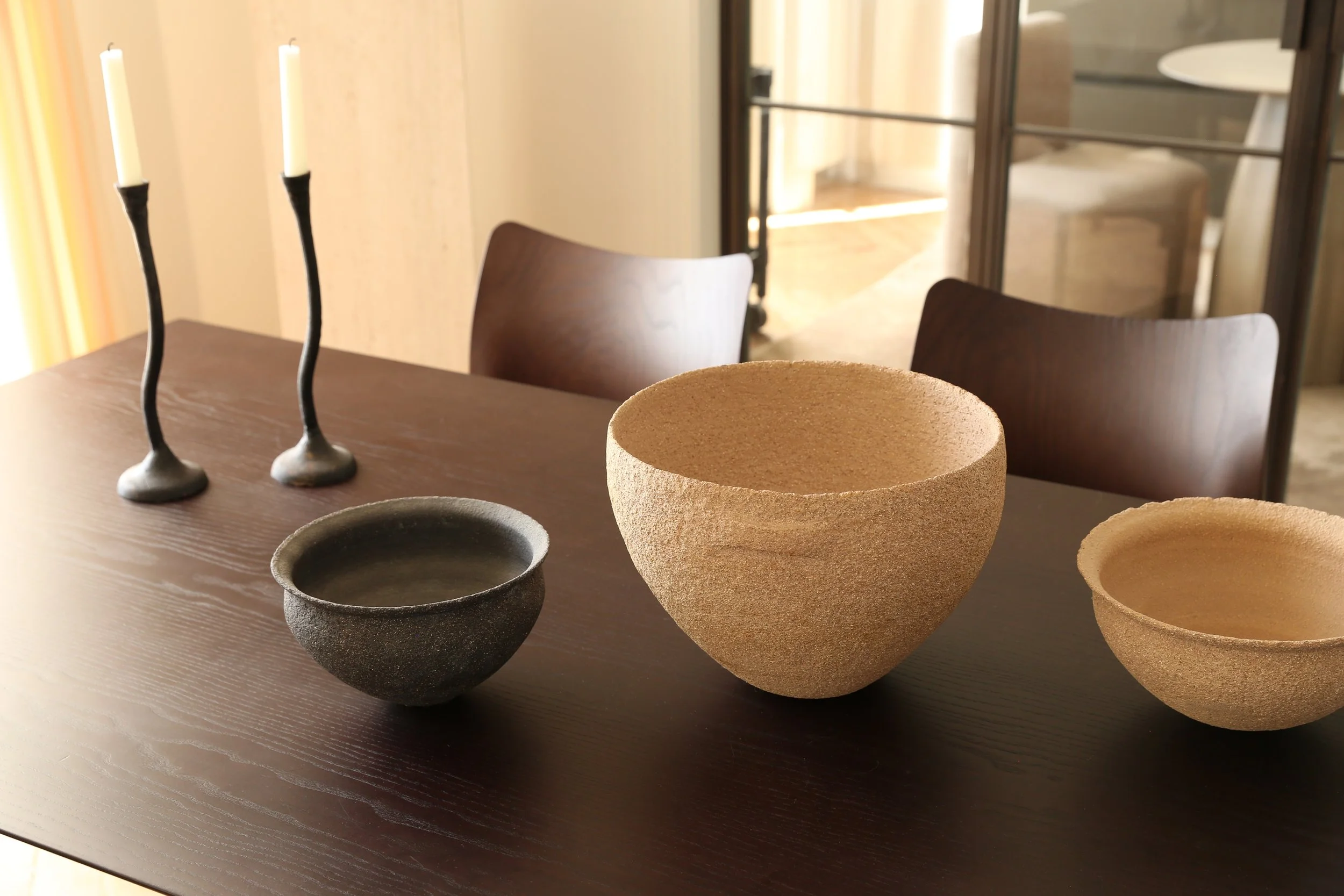Varios recipientes de cerámica en diferentes tamaños y colores en una mesa de madera, con una llama de velas encendida en el fondo.