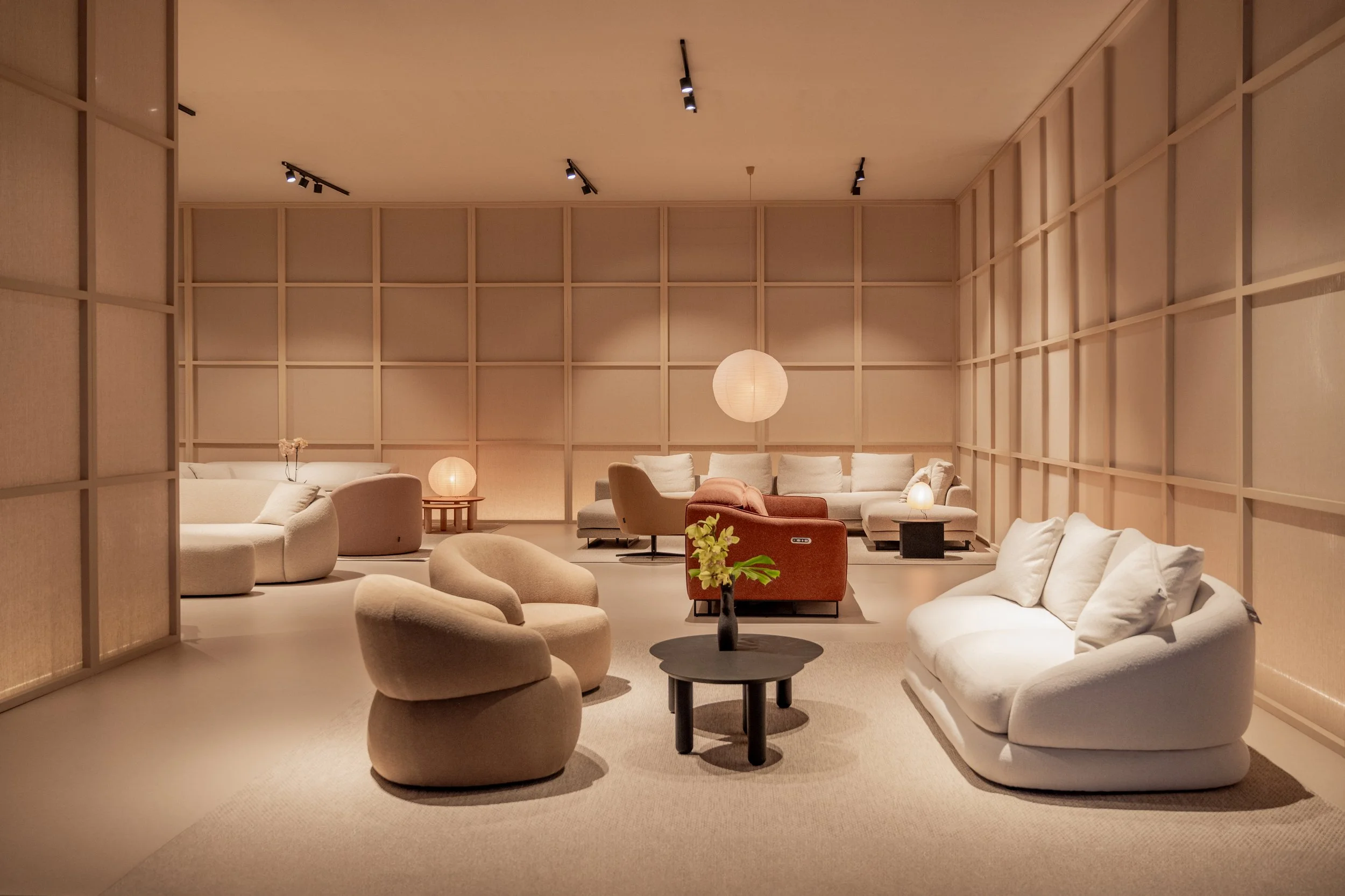 Sala de estar con sillones y mesas elegantes, decorada con lámparas de papel y una pared de madera en el fondo, ambiente cálido y moderno.