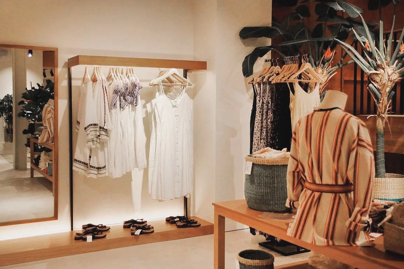 Ropa de verano en una boutique, incluyendo camisetas, vestidos y sandalias, con decoración en tonos neutros y plantas decorativas.