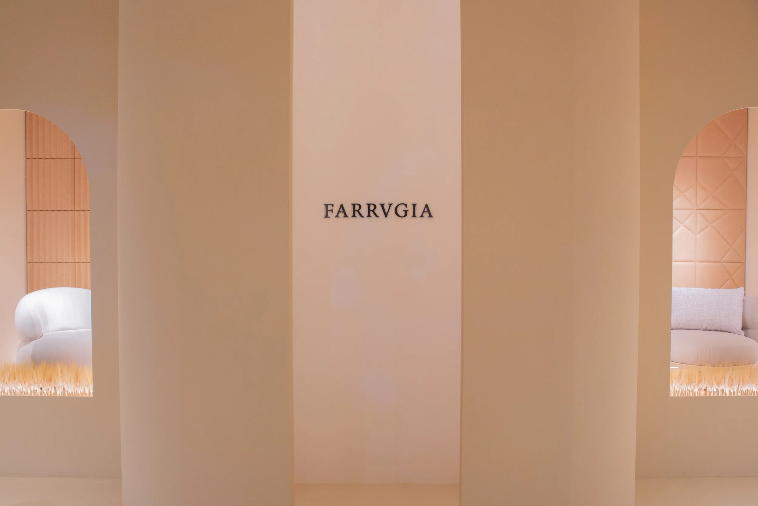 Un espacio interior con paredes en tonos neutros, decorado con muebles blancos, una alfombra beige y cojines en tonos claros, con un cartel que dice 'FARRVGIA' en el centro.