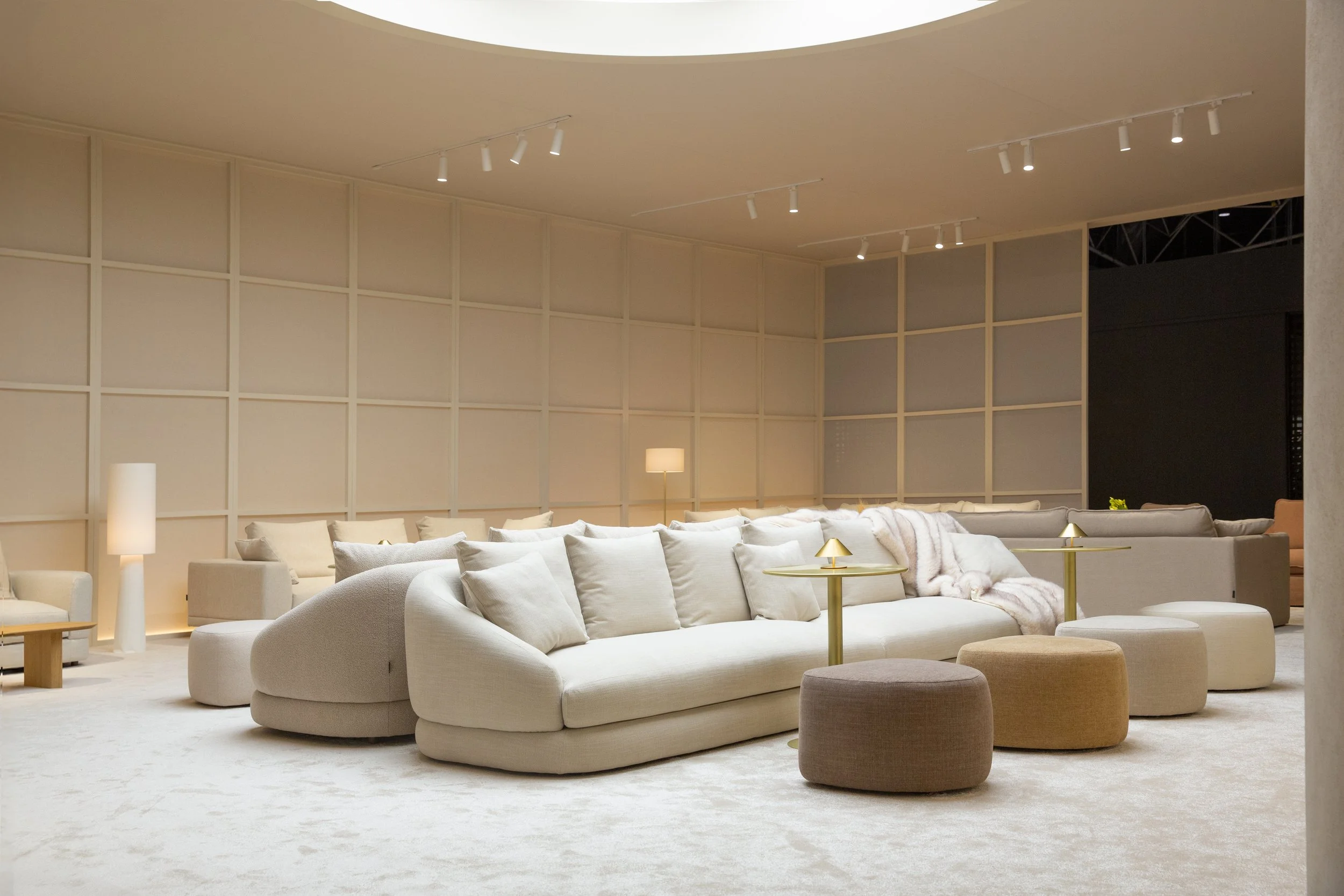 Hábitat Valencia. Stand Temasdos con sillones blancos, mesitas doradas, lámparas de mesa, alfombra beige y paredes decoradas con paneles