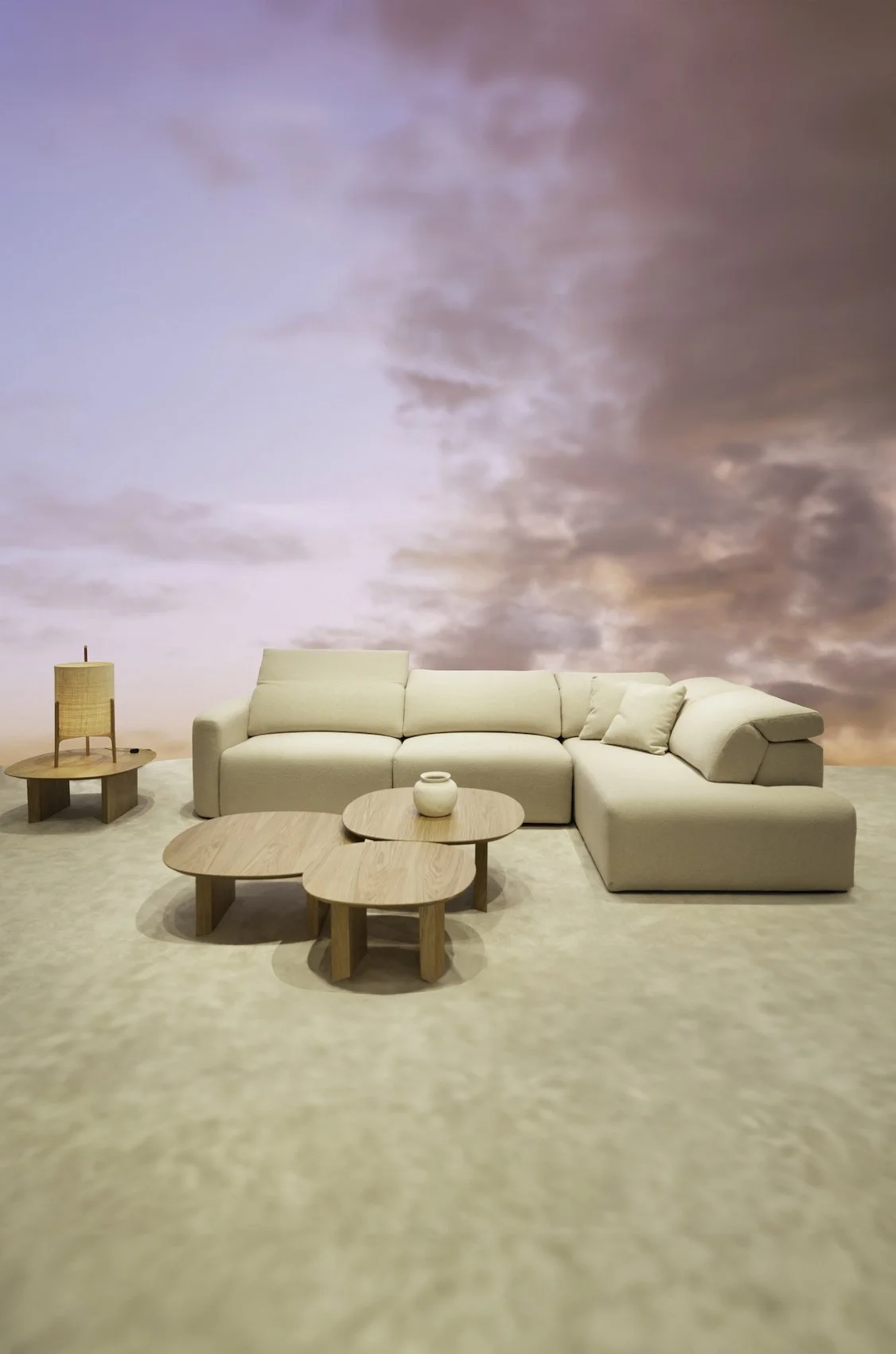 Sofá blanco en una sala con mesa de madera y lámpara sobre fondo de cielo rosado con nubes.