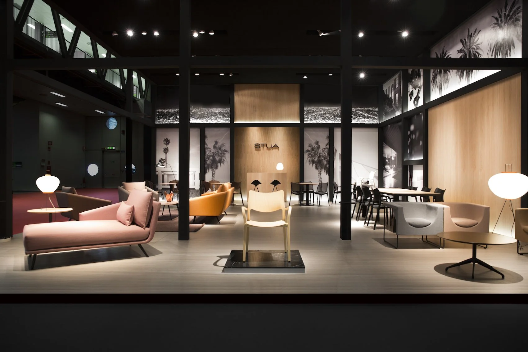 Interior elegante de un lounge con sillones y mesas, paredes decoradas con fotos en blanco y negro de palmeras y ciudad, iluminación suave, y la palabra 'STUA' en una pared de madera en el fondo.