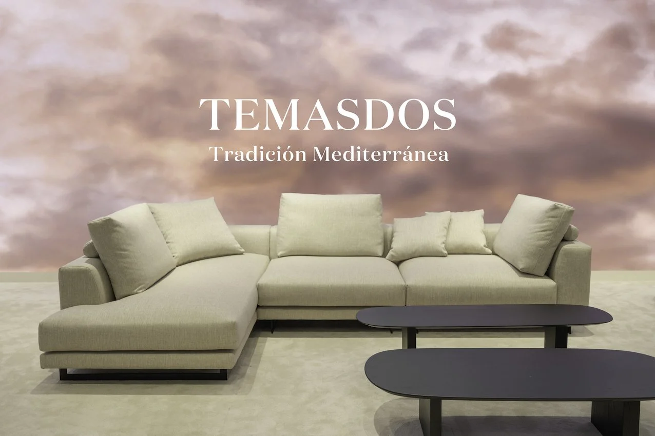 Mensaje: Temasdos, Tradición Mediterránea, sofá beige con cojines y mesas negras en un salón con pared decorativa con cielo rosado