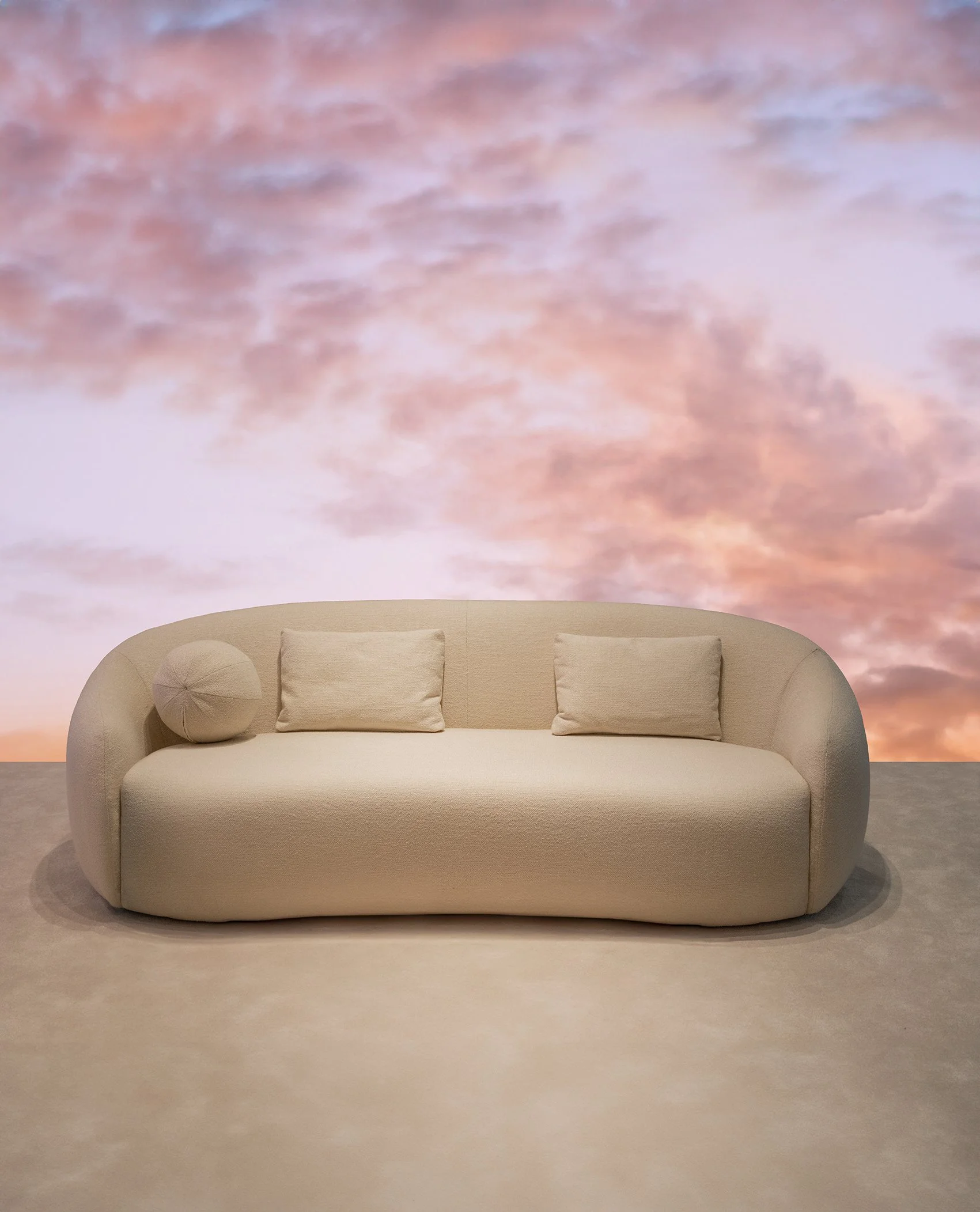 Sofá beige moderno con dos cojines, frente a un mural que simula un cielo con nubes rosadas y lilas