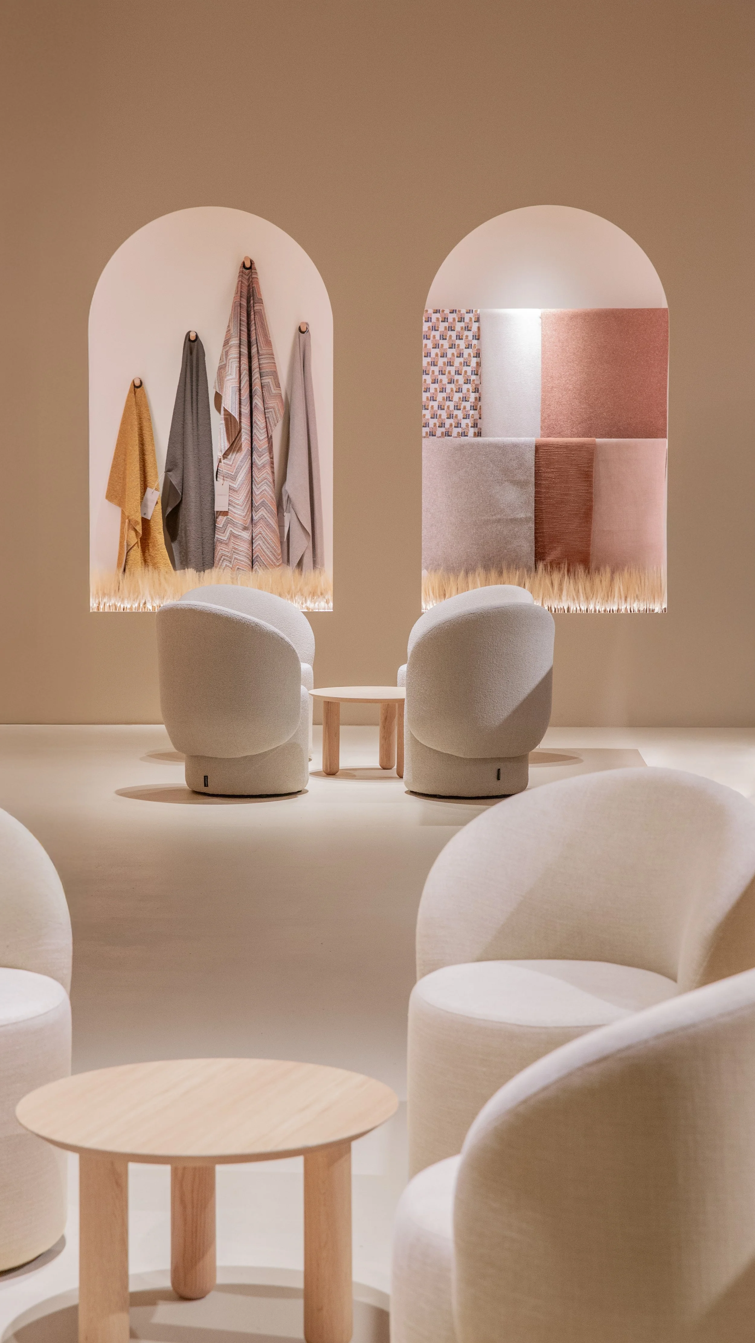 Sala de espera moderna con sillones blancos y mesas de madera, paredes decoradas con tejidos de colores suaves y textiles con patrones geometricos y texturas variadas.