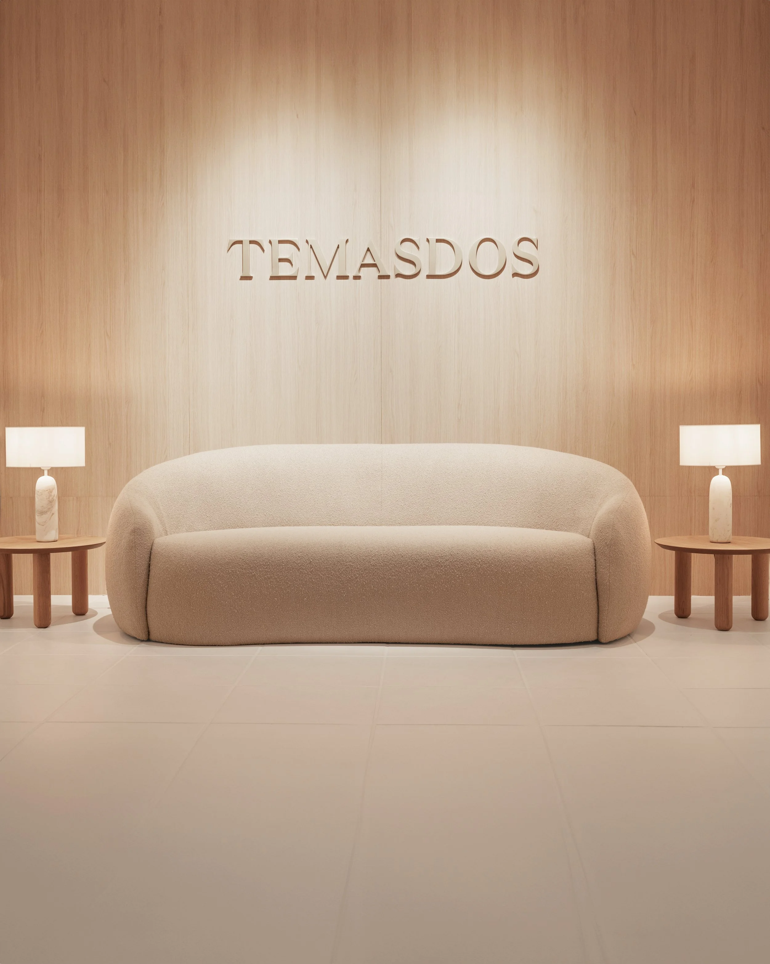 Sala elegante con pared de madera clara, lámparas en mesas de madera, sofá beige y cartel que dice 'Temasdos' en la pared.