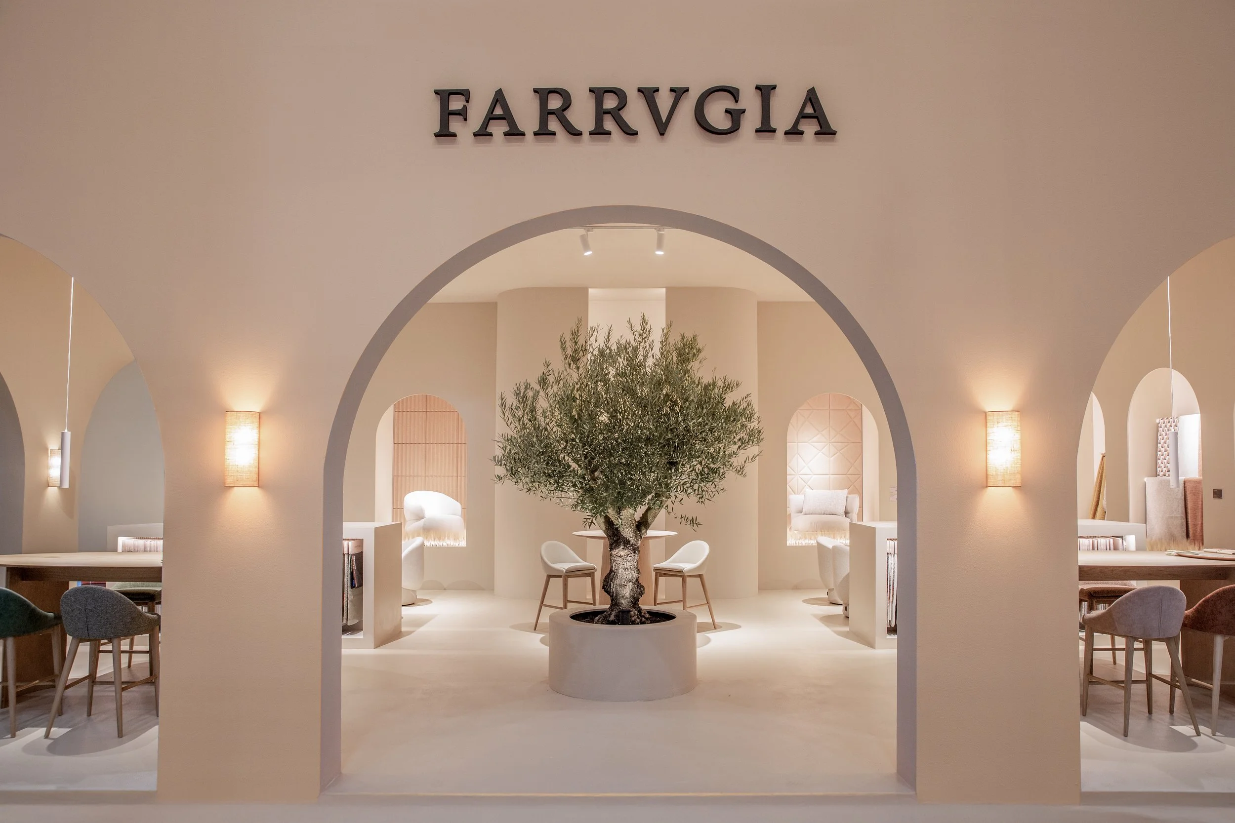 Interior elegante con un árbol en una maceta grande en el centro, sillones blancos, paredes iluminadas y el letrero 'FARRVGIA' en la pared del fondo.