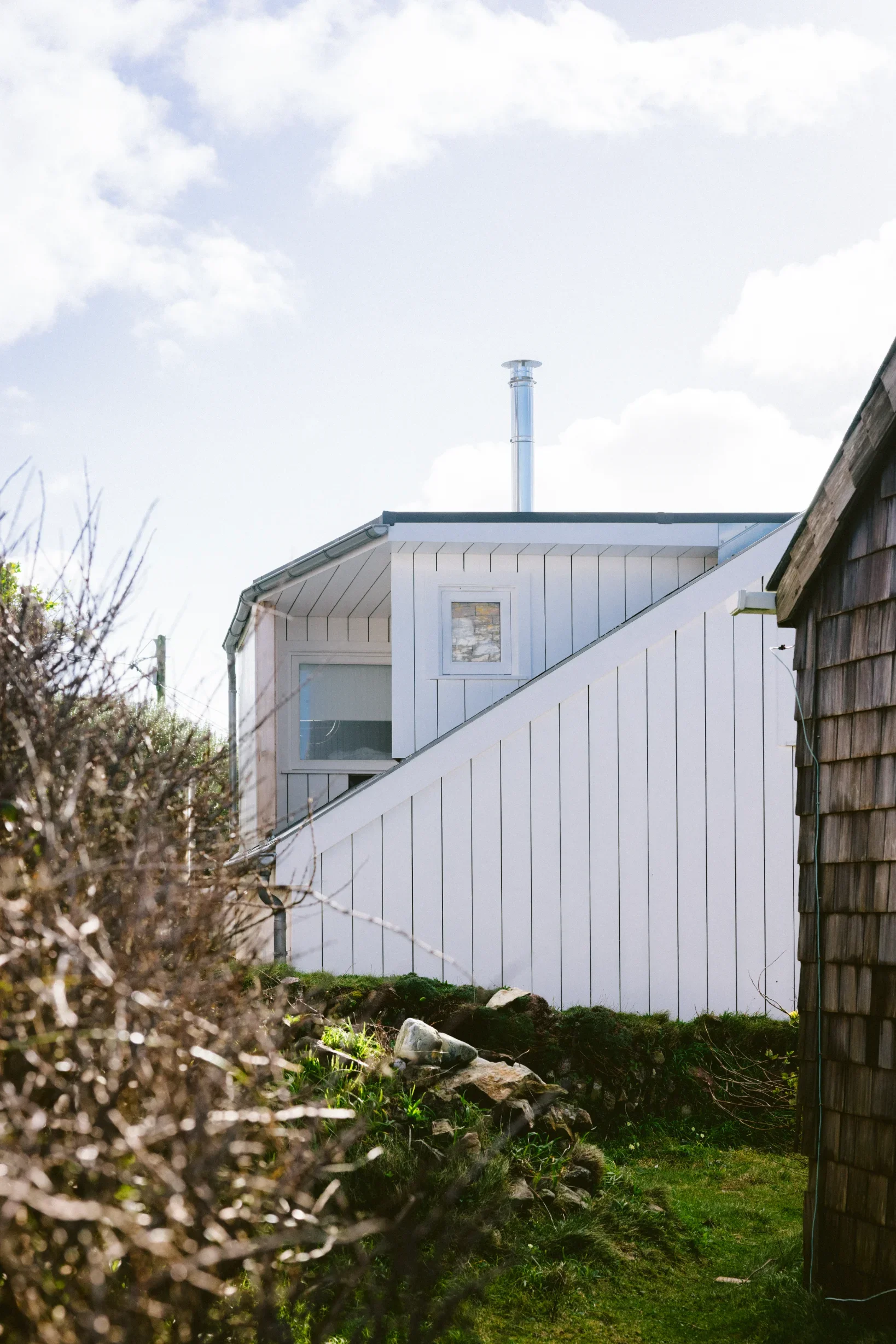 Exterior side elevation of converted coastal structure, white vertical timber cladding and metal flue, Chapel Porth Cornwall