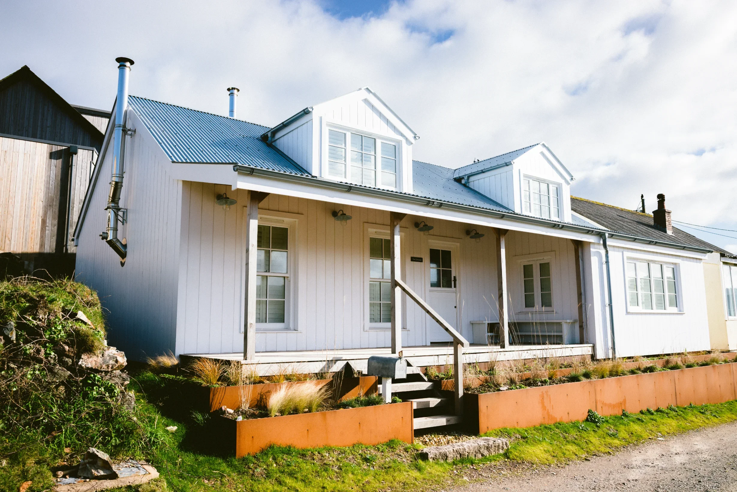 Converted First World War coastal structure at Chapel Porth, white timber cladding, corrugated metal roof and Corten steel raised beds, Elements Build Cornwall