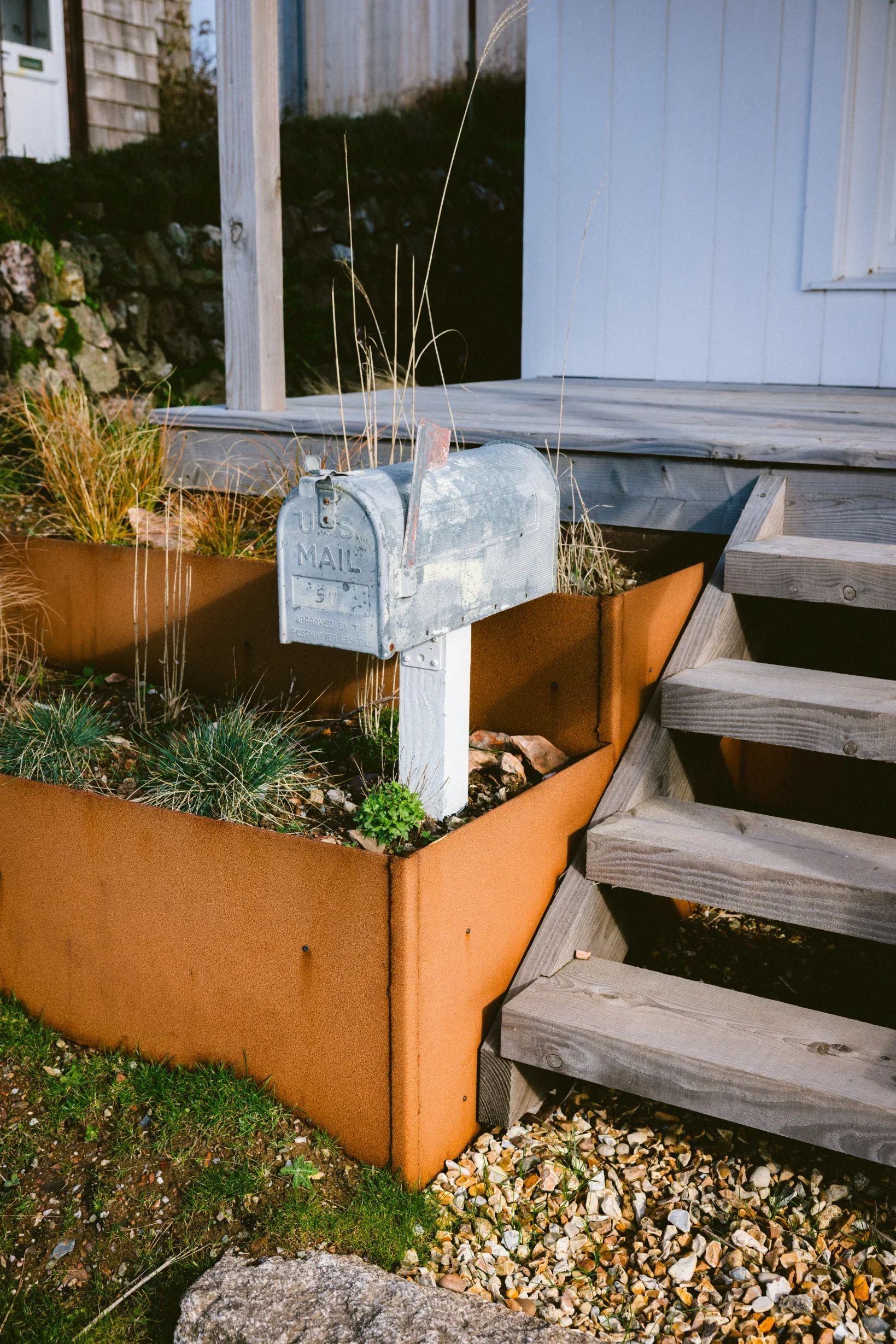 Corten steel raised beds with coastal grasses flanking timber veranda steps, Chapel Porth conversion, Elements Build and Marrum Architects