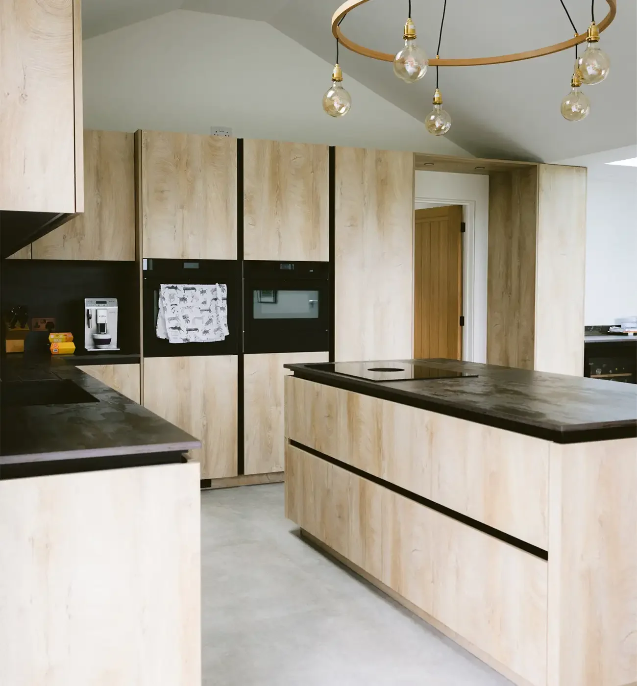 Completed kitchen interior with vaulted ceiling, light oak cabinetry, dark stone worktops and polished concrete floor, built by Elements Build Cornwall