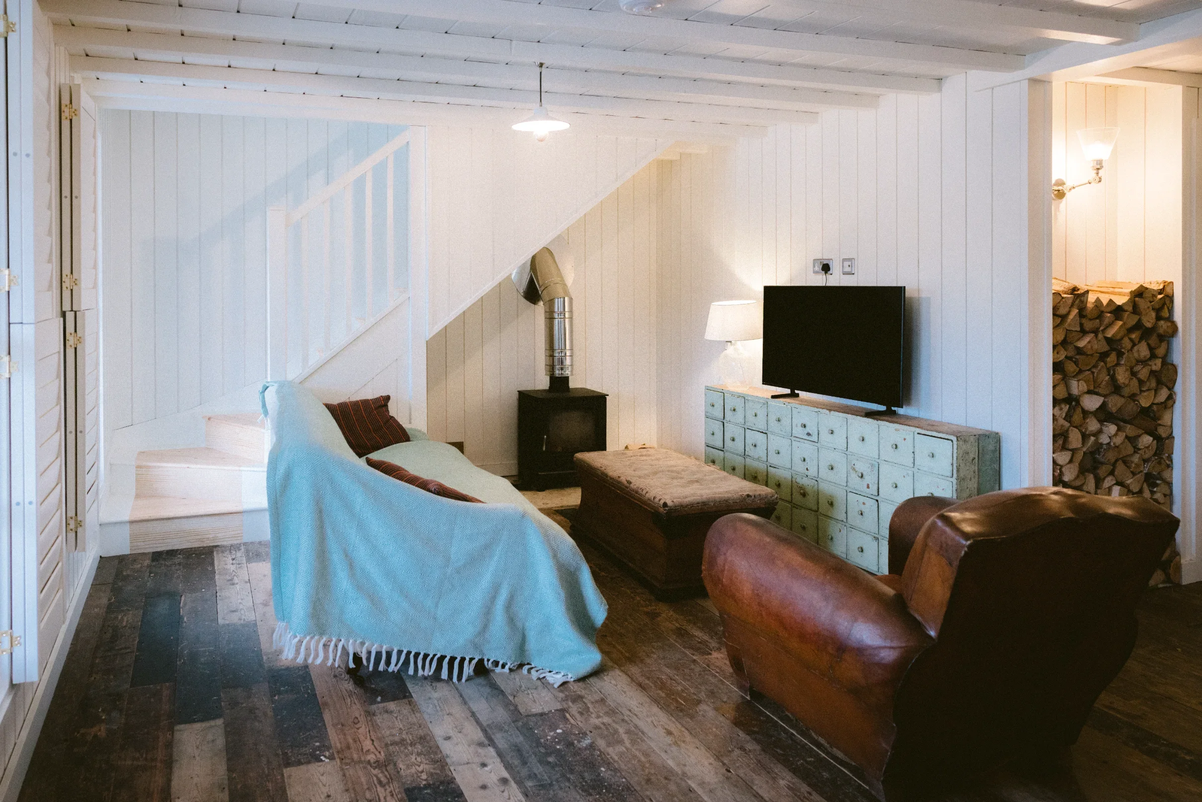 Living room with wood-burning stove, reclaimed timber floor and white-painted staircase, airtight conversion Chapel Porth Cornwall