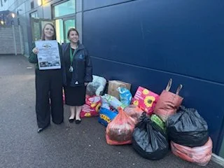 Two women standing next to a pile of bags and donations outside a building.