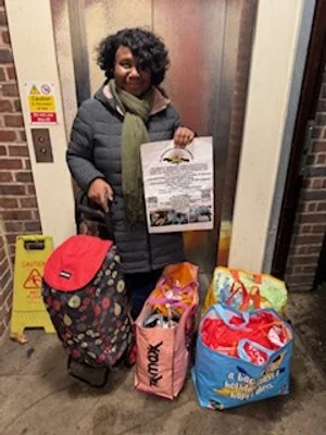 Woman standing in an elevator holding a bag, with several shopping bags and a rolling suitcase with a floral pattern in front of her.