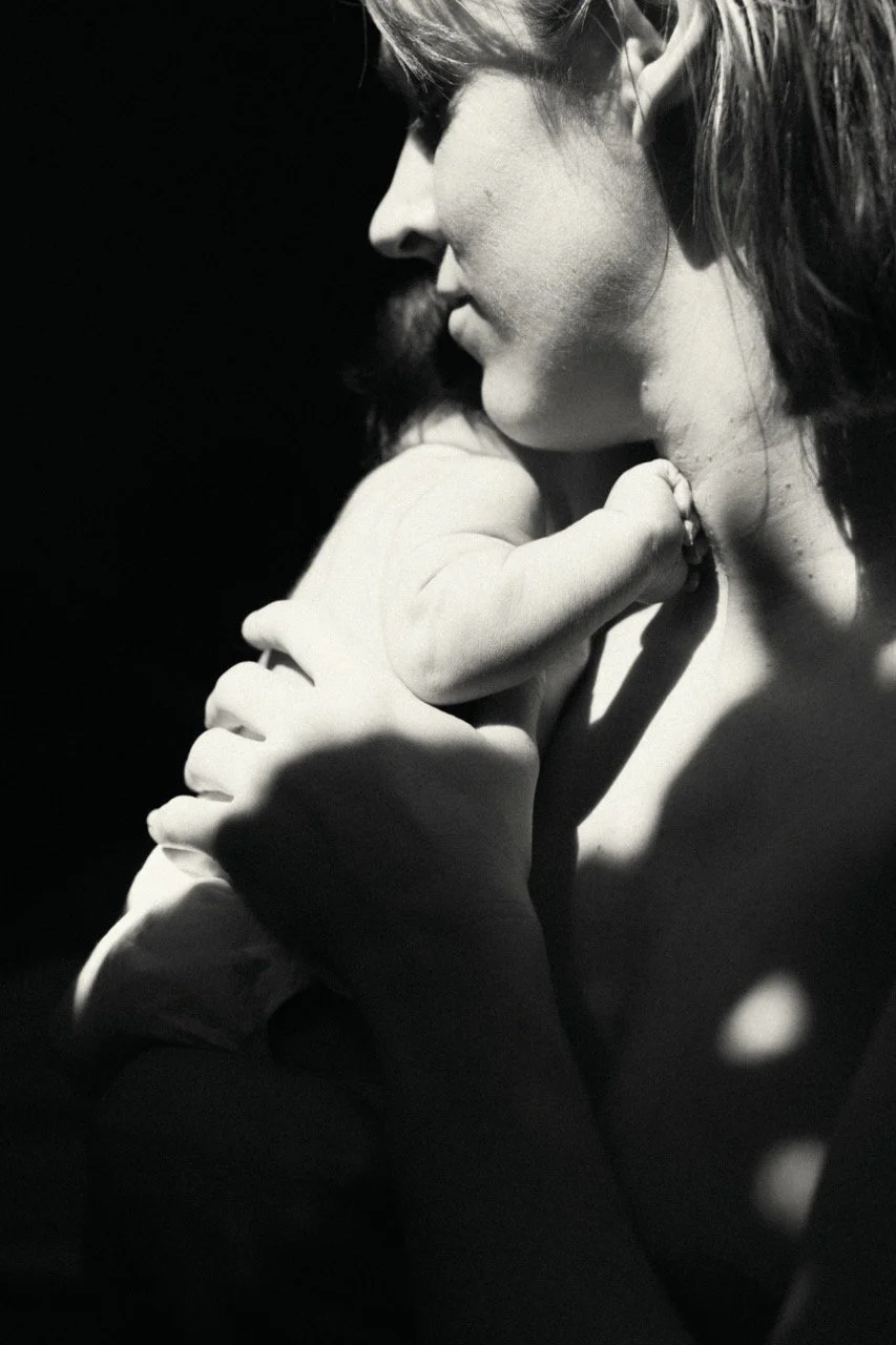 An intimate black and white portrait of a mother holding her newborn baby, highlighting the raw emotion and connection of the postpartum period.
