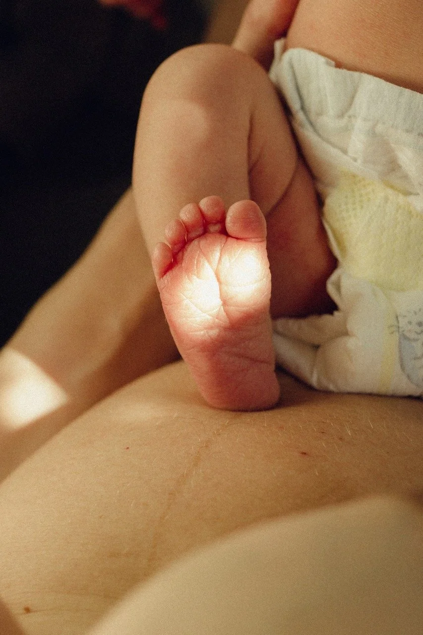 Newborn's tiny feet resting on a mother's skin — a quiet detail from the early days. Intimate newborn photography in Tokyo capturing what is often unseen.