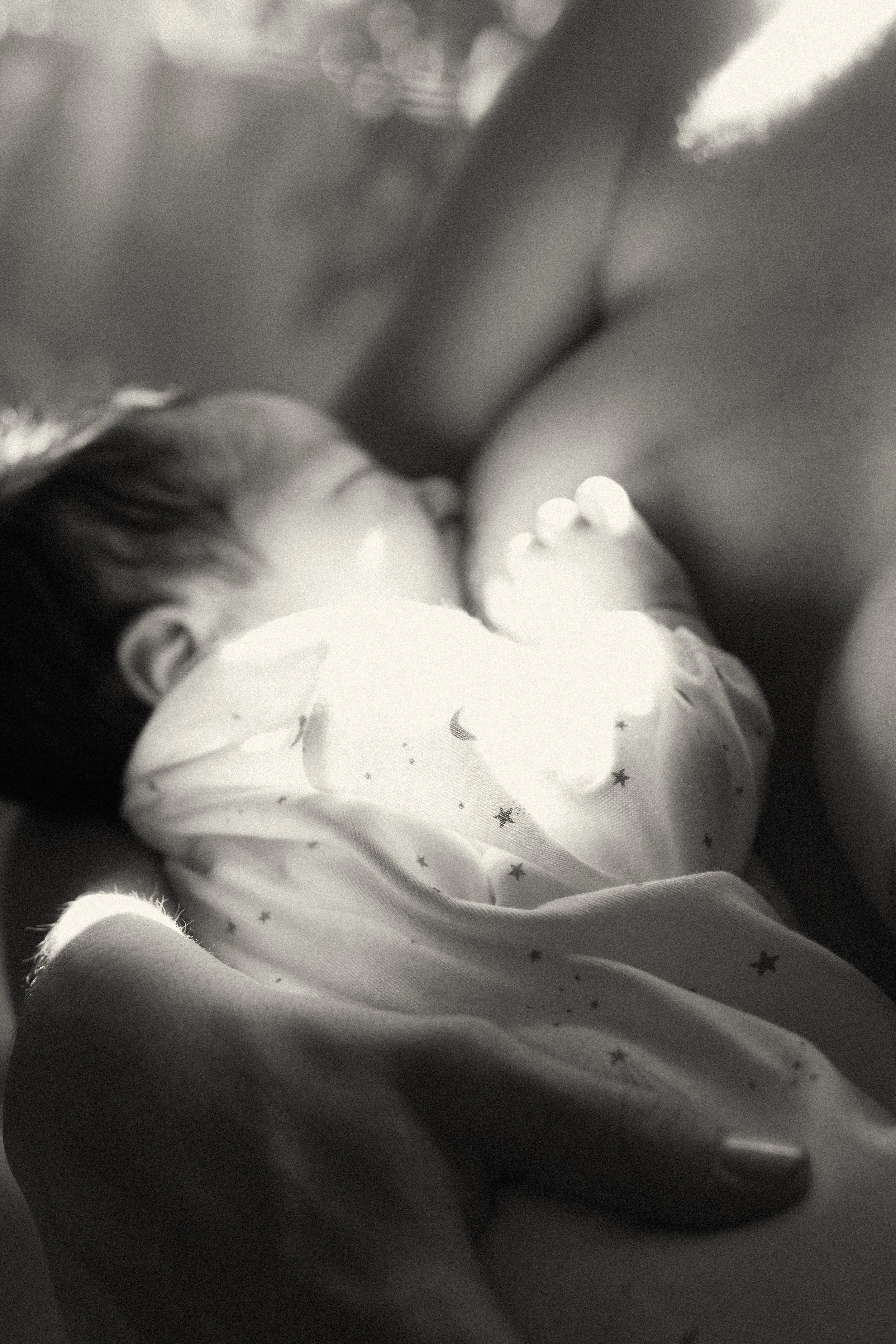 Black and white photograph of a newborn breastfeeding with high-contrast lighting and film grain