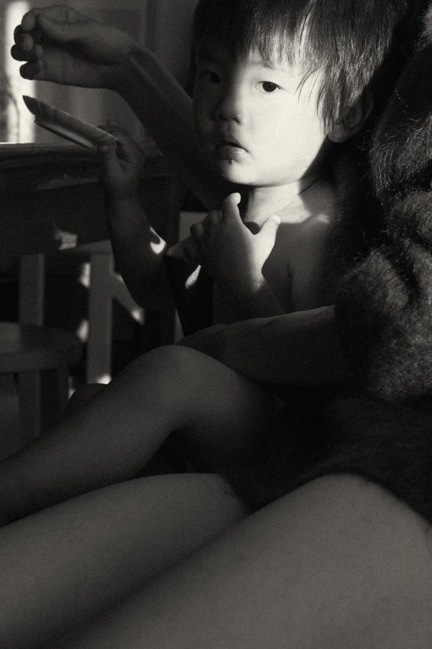 Intimate black and white portrait of a young child being held by mother in golden light — a still, observant moment captured during a family lifestyle session in Tokyo focusing on motherhood tenderness and childhood memory