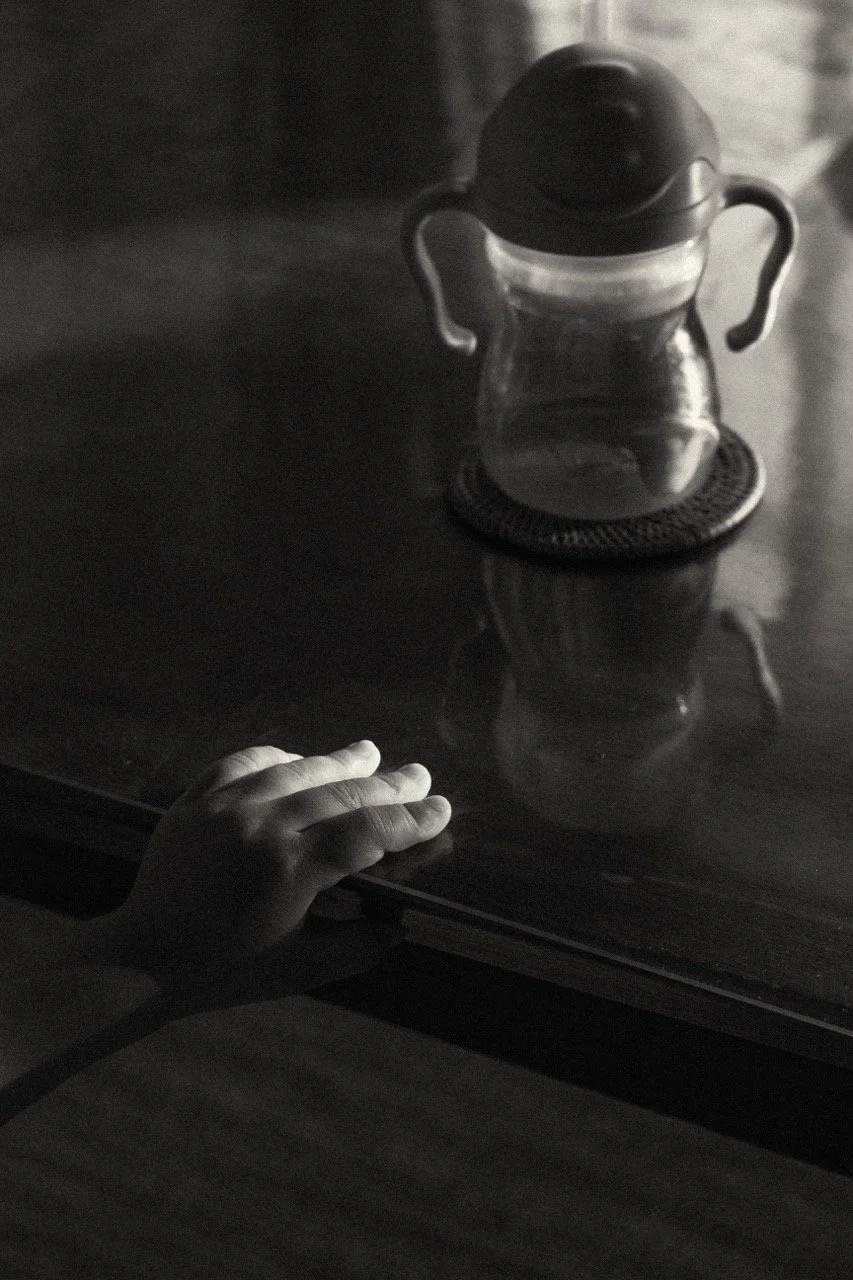 A child's small hand reaching toward a bottle water on the table — a quiet everyday detail from a family lifestyle session focusing on childhood memory in Tokyo by Noa Nguyen.