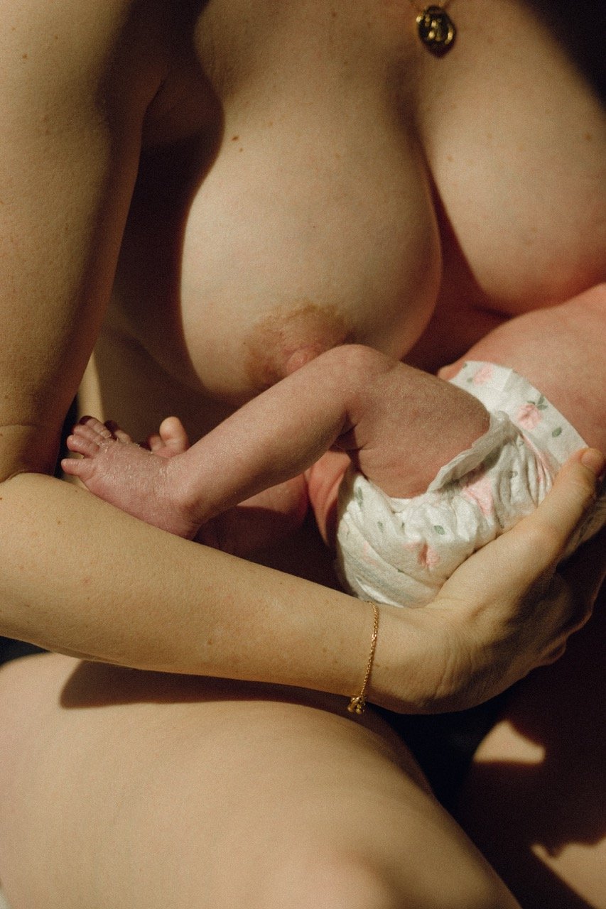 A mother holds her newborn against her bare chest — skin to skin contact in the early days of motherhood. Honest newborn photography in Tokyo by Noa Nguyen.