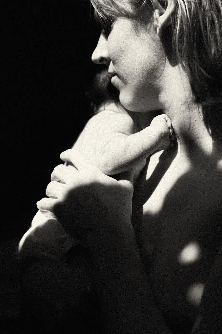 Black and white portrait of a mother holding her newborn at home in morning light — the invisible love of early motherhood, unposed and real. English speaking newborn family photographer in Tokyo.