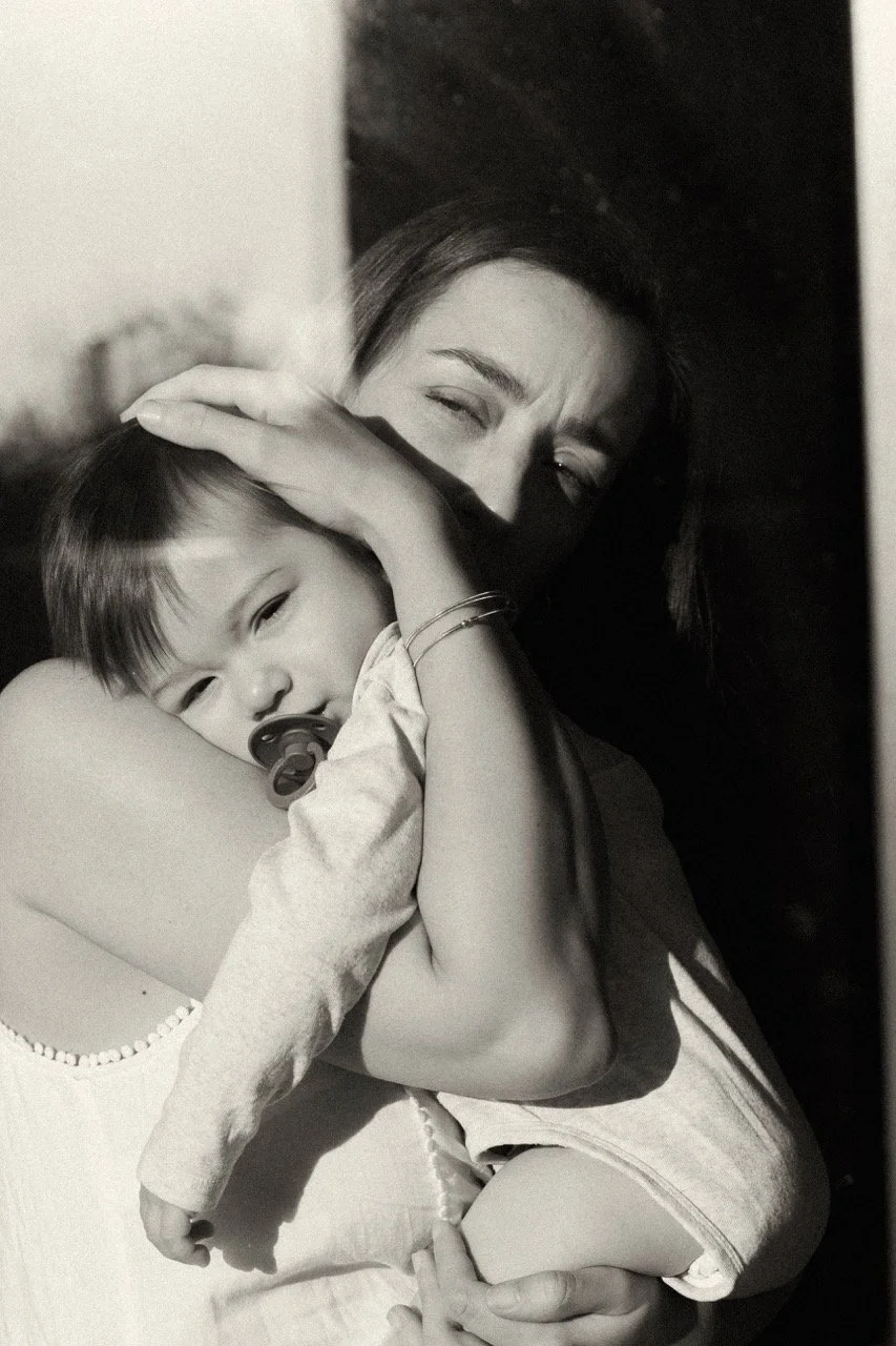 black and white documentary photography of an exhausted mother holding her sleepy baby close. the real, unposed tenderness of new motherhood. Intimate newborn and family lifestyle photography by Noa Nguyen available for expat families.