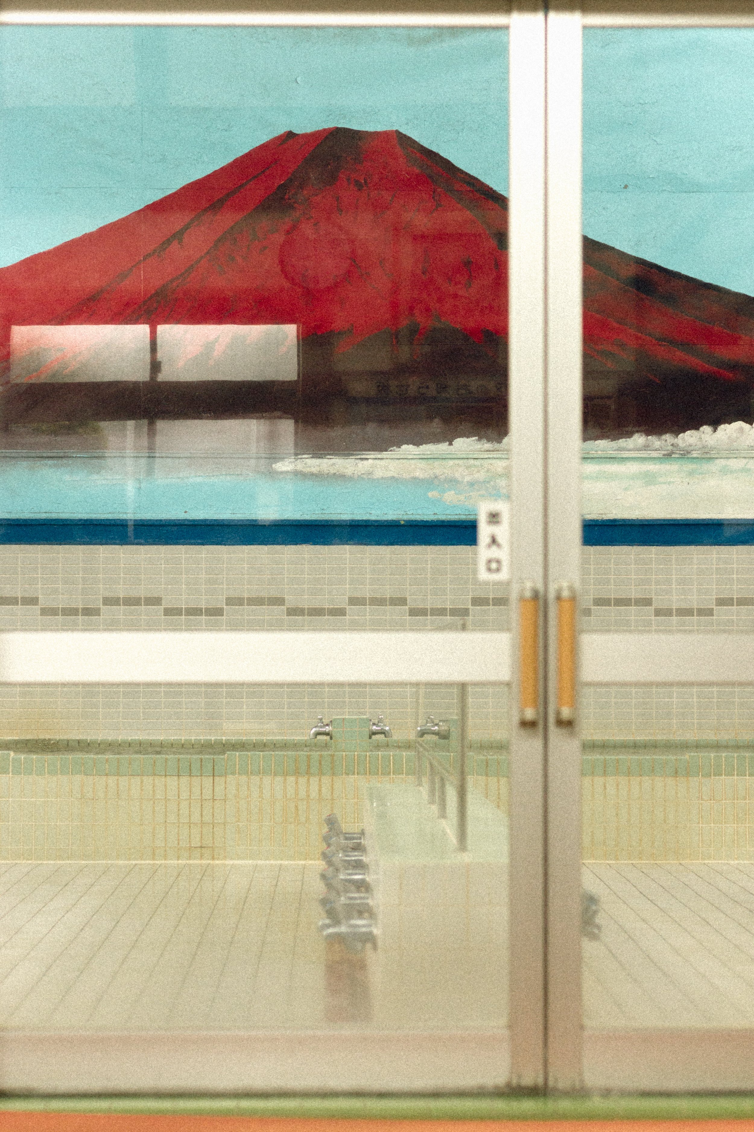 A poetic film photograph of a red Mount Fuji mural inside a traditional Japanese sento, anchoring the photography service in Tokyo's culture.
