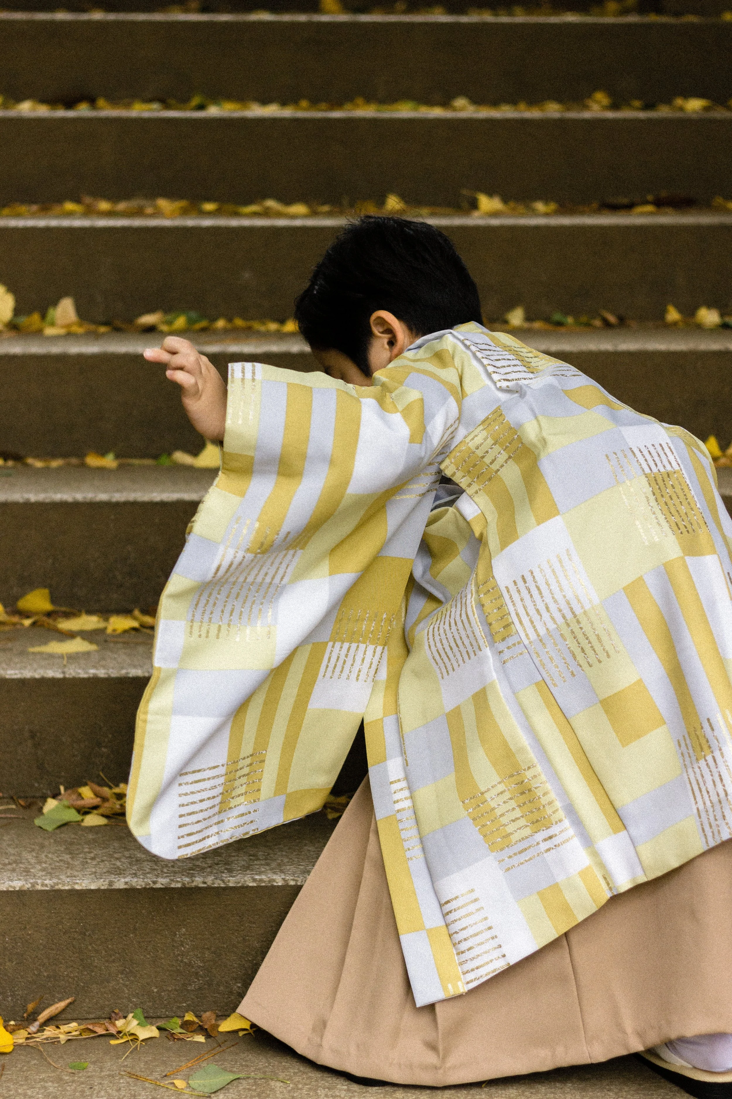 A candid color photograph of a young boy in a traditional kimono climbing stone shrine steps, focusing on movement and authentic celebration.