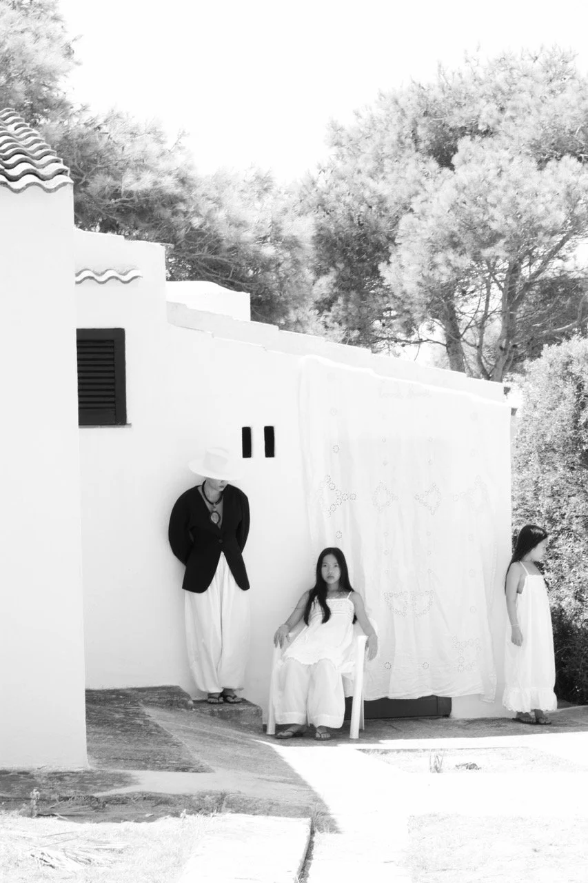 Wide shot of a mother and her two daughters in a sun-drenched courtyard — a stylish family portrait with an editorial feel. Family lifestyle photography by Noa Nguyen in Paris
