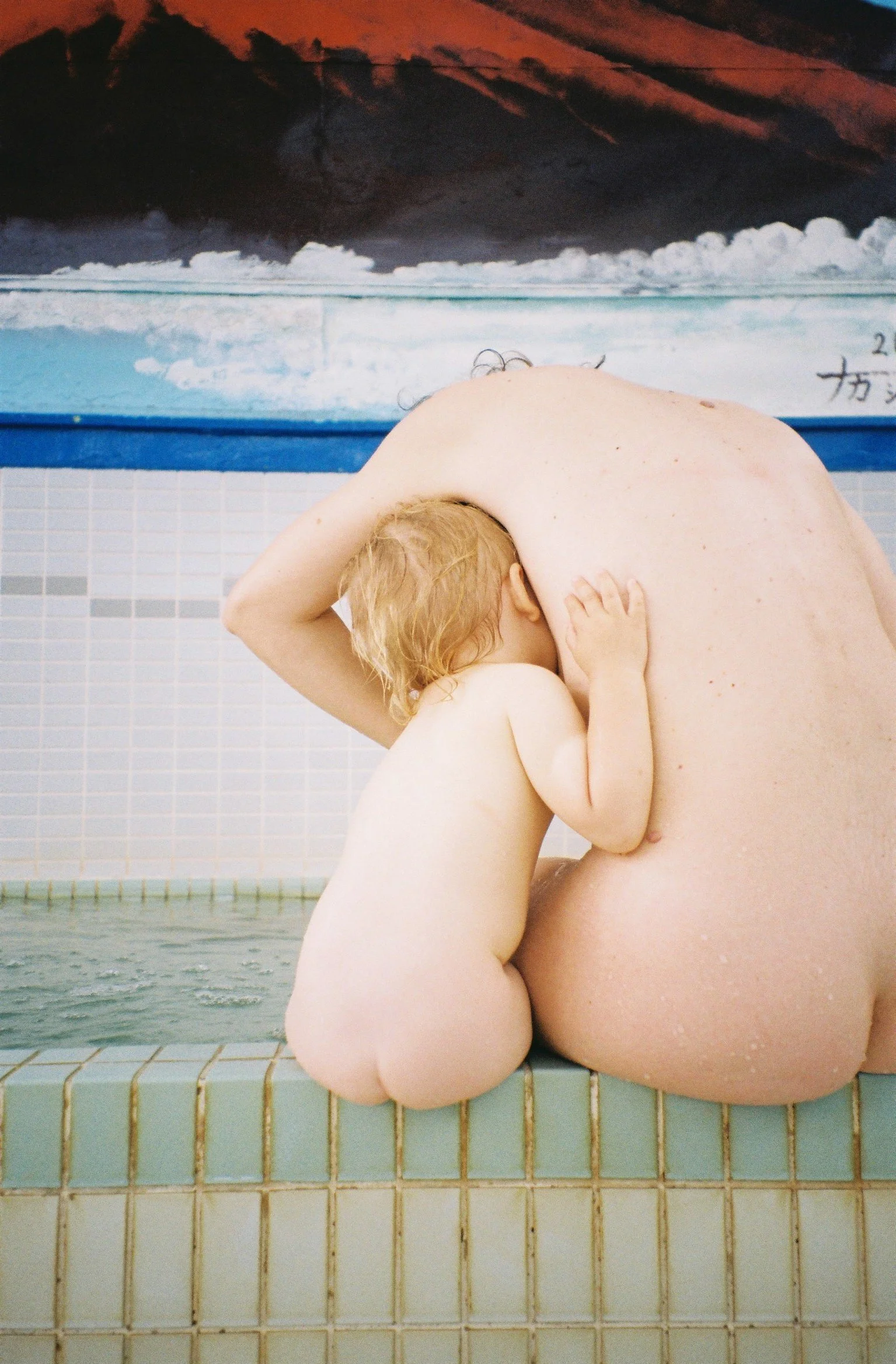 An intimate motherhood portrait in a Japanese sento, capturing a skin-to-skin breastfeeding moment between mother and baby in a raw film style.