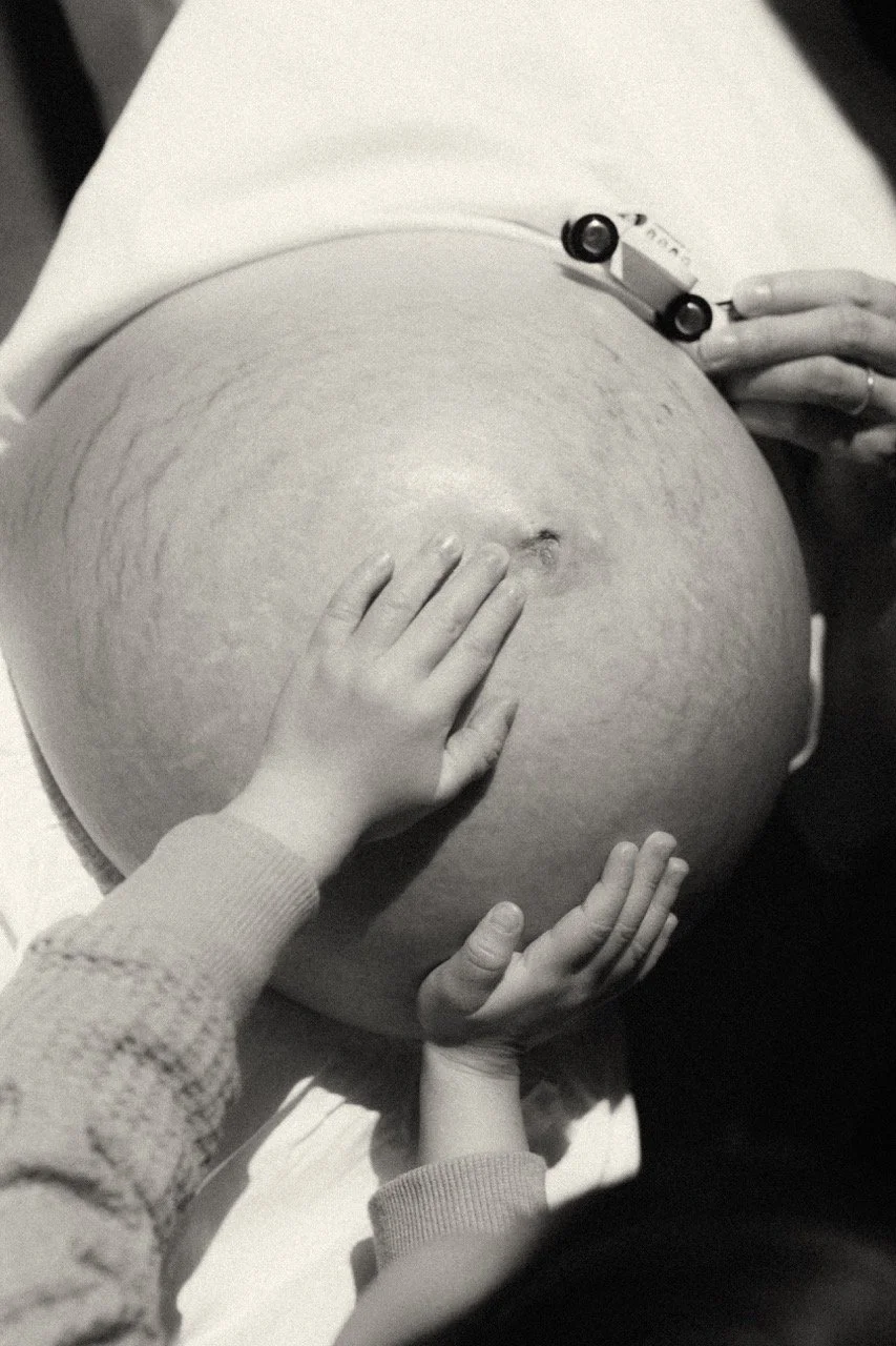 A toddler's small hands touch her mom pregnancy belly covered in stretch marks — an honest maternity photograph capturing the sibling transition and unseen strength of mother . Family photographer in Tokyo.