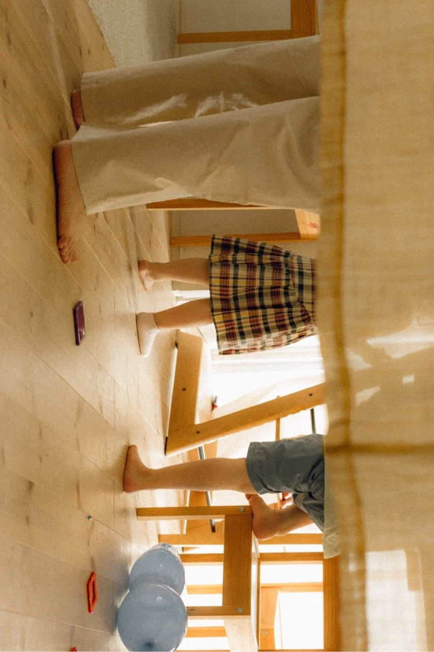 A playful afternoon photograph showing the lower half of a family in their Tokyo home, capturing a candid and messy moment of daily life with toddlers.