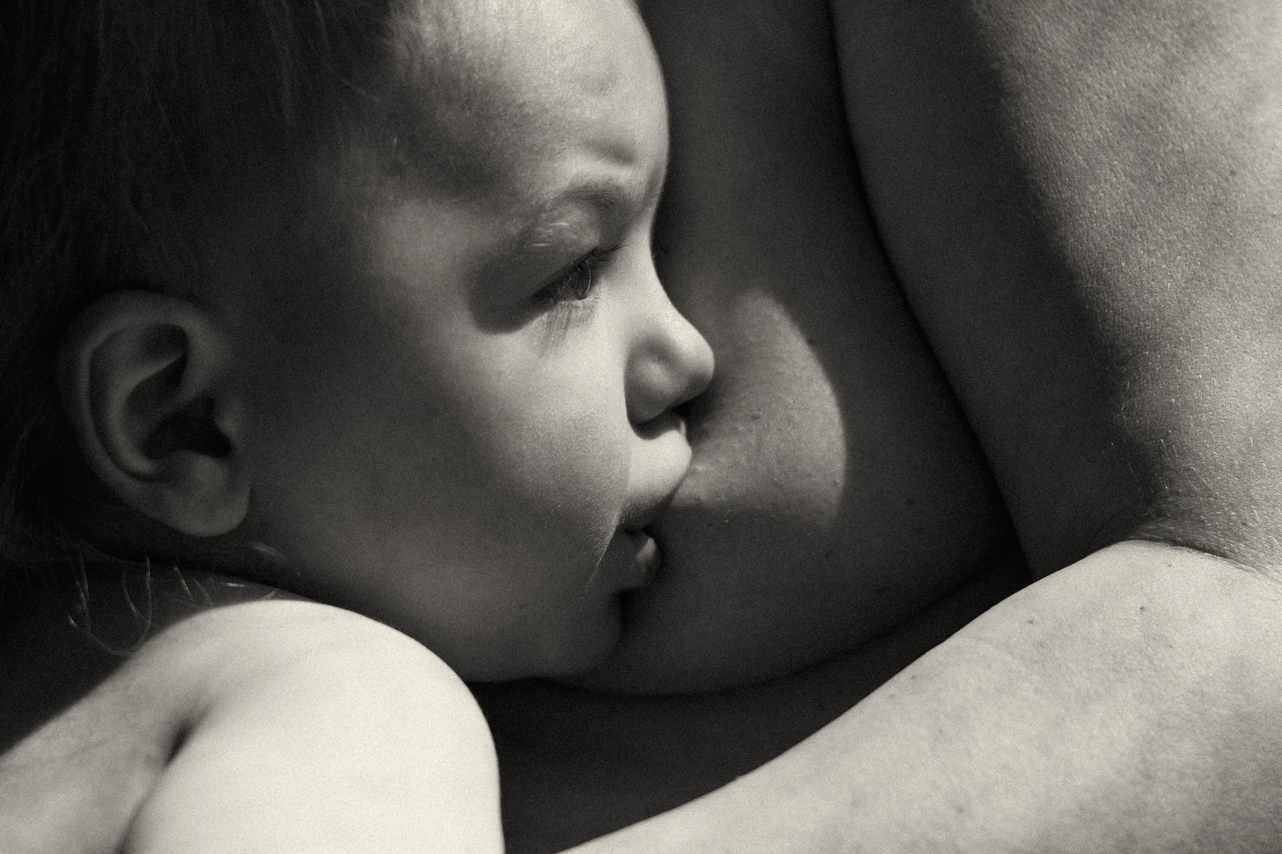Close up black and white photograph of a baby breastfeeding — tender, intimate skin to skin contact captured by English speaking newborn photographer Noa Nguyen in Tokyo.