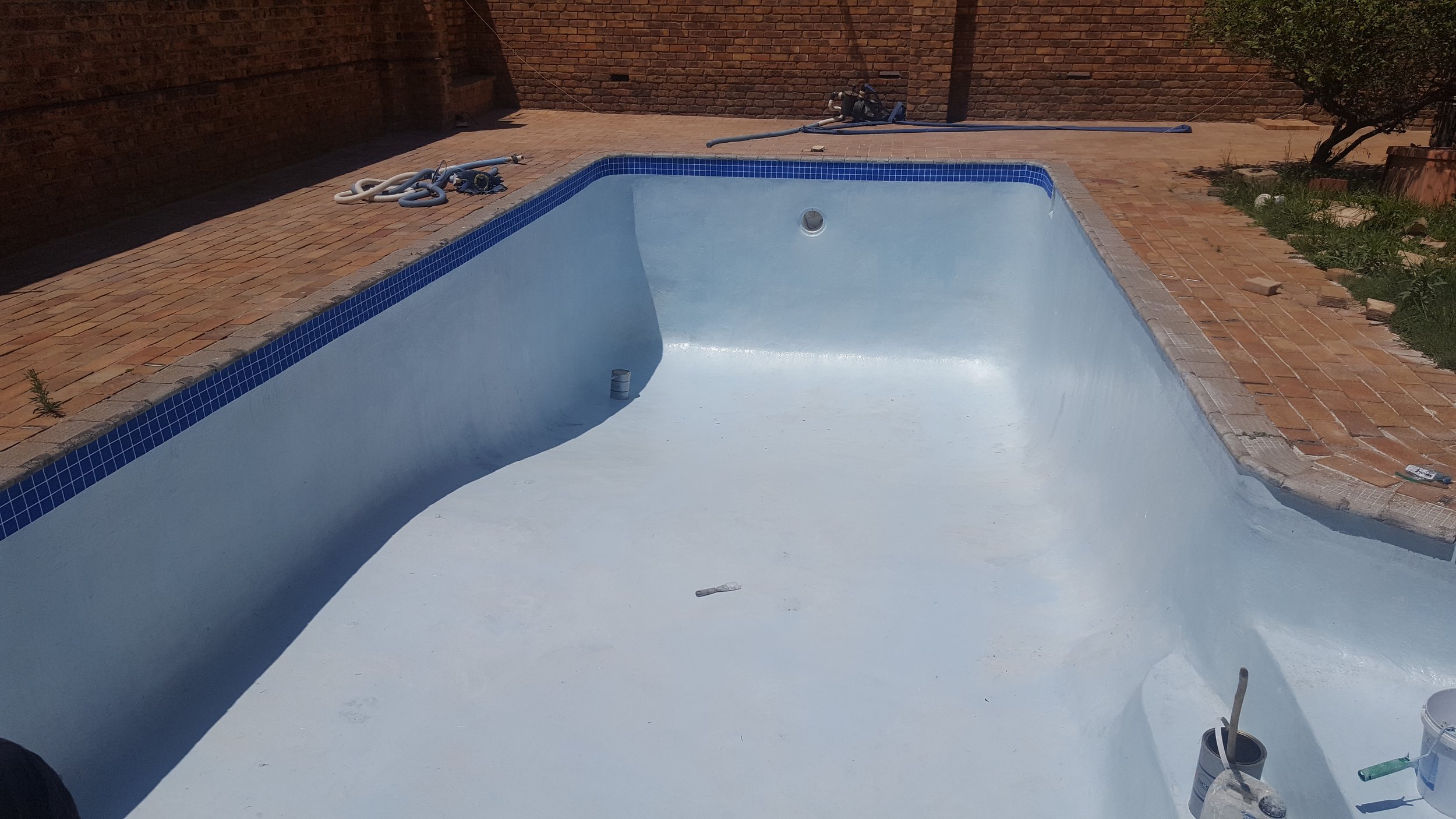Empty swimming pool under maintenance with cleaning equipment on the poolside.