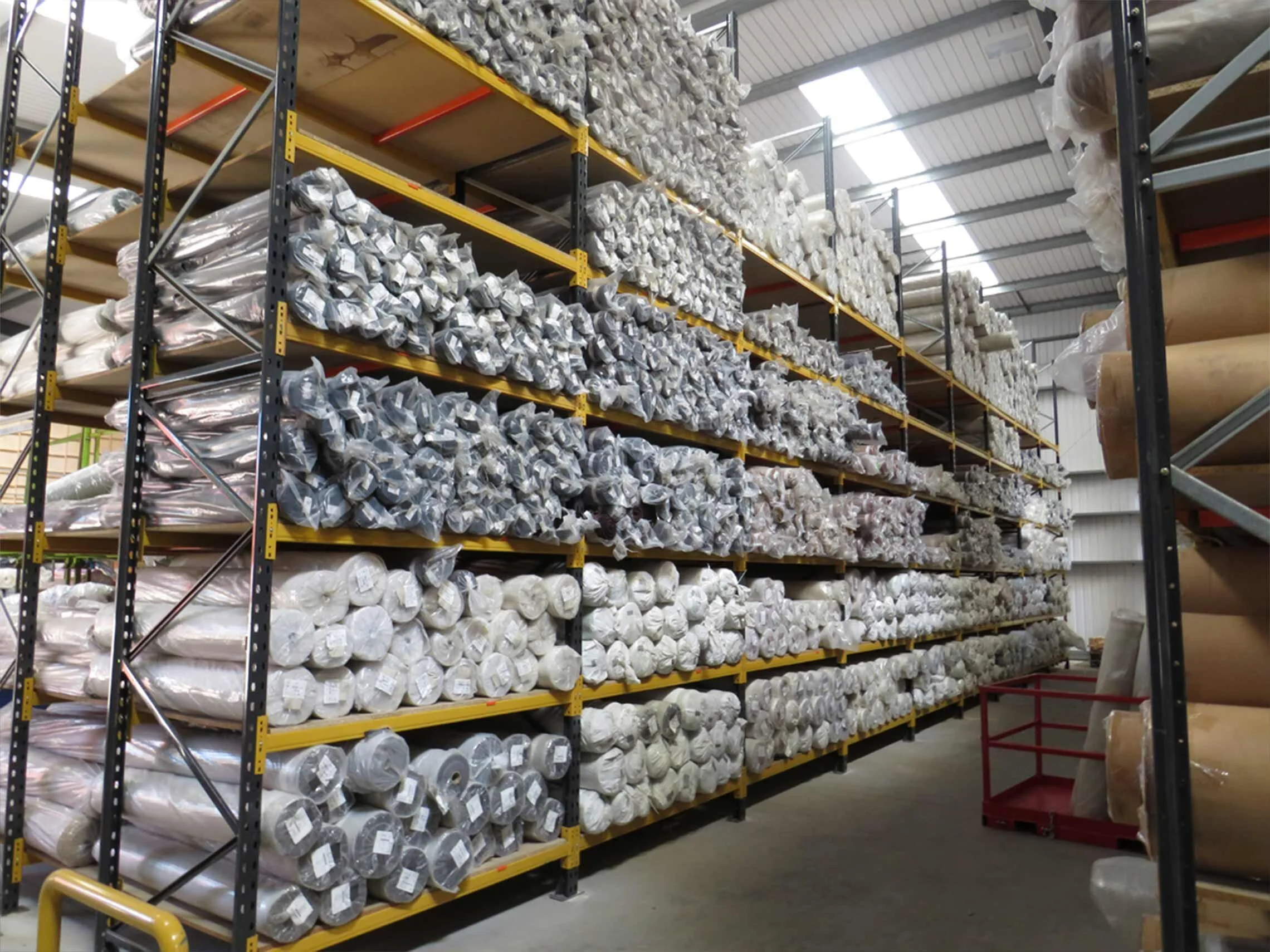 Warehouse with shelves storing large rolls of fabric wrapped in plastic.