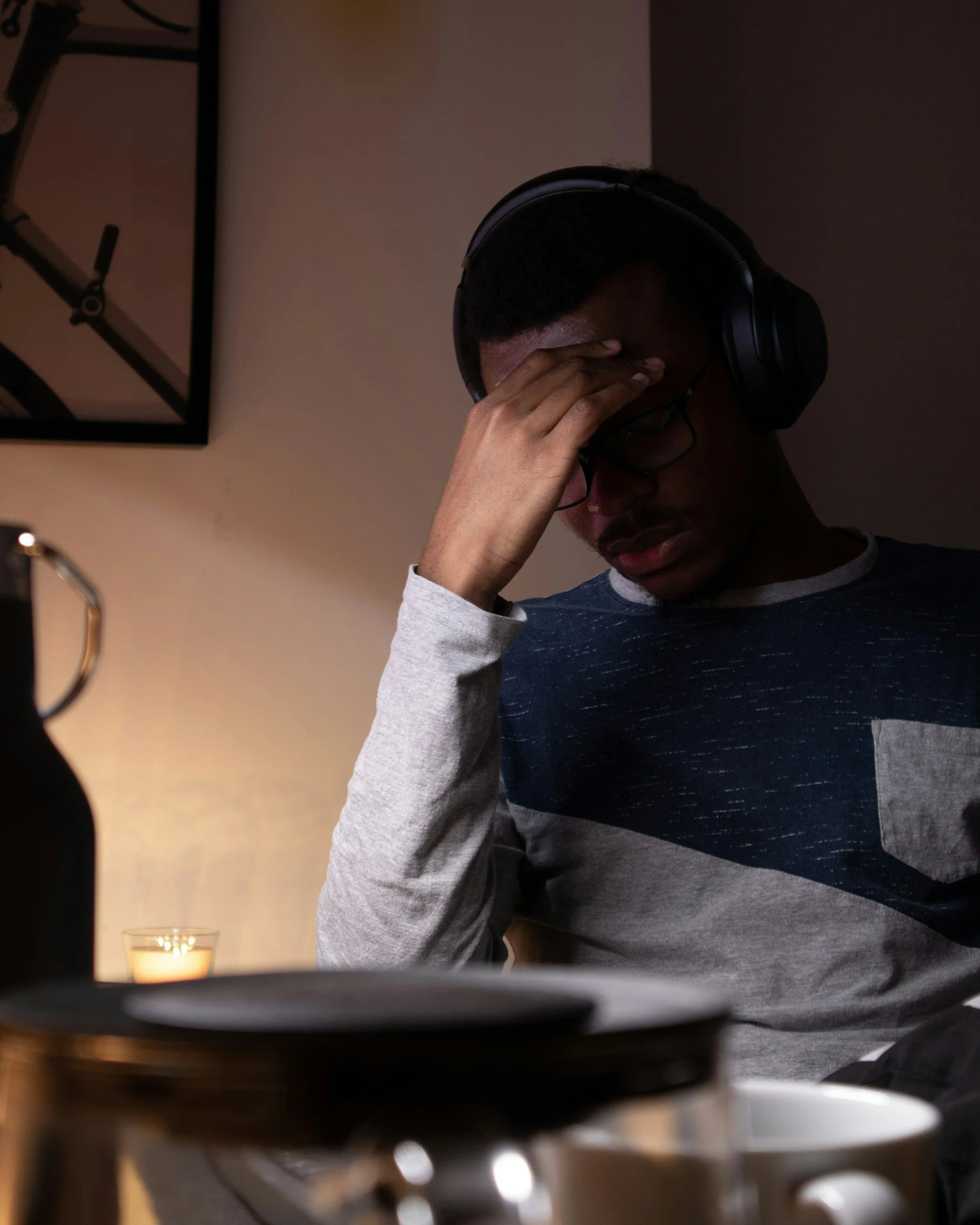 Image of black man with headphones and glasses leaning his head forward, looking tired