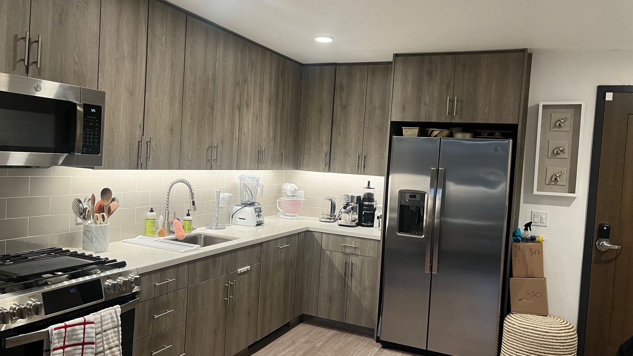 Modern kitchen with gray cabinets, stainless steel appliances, and countertop cluttered with small appliances like a toaster and blender.