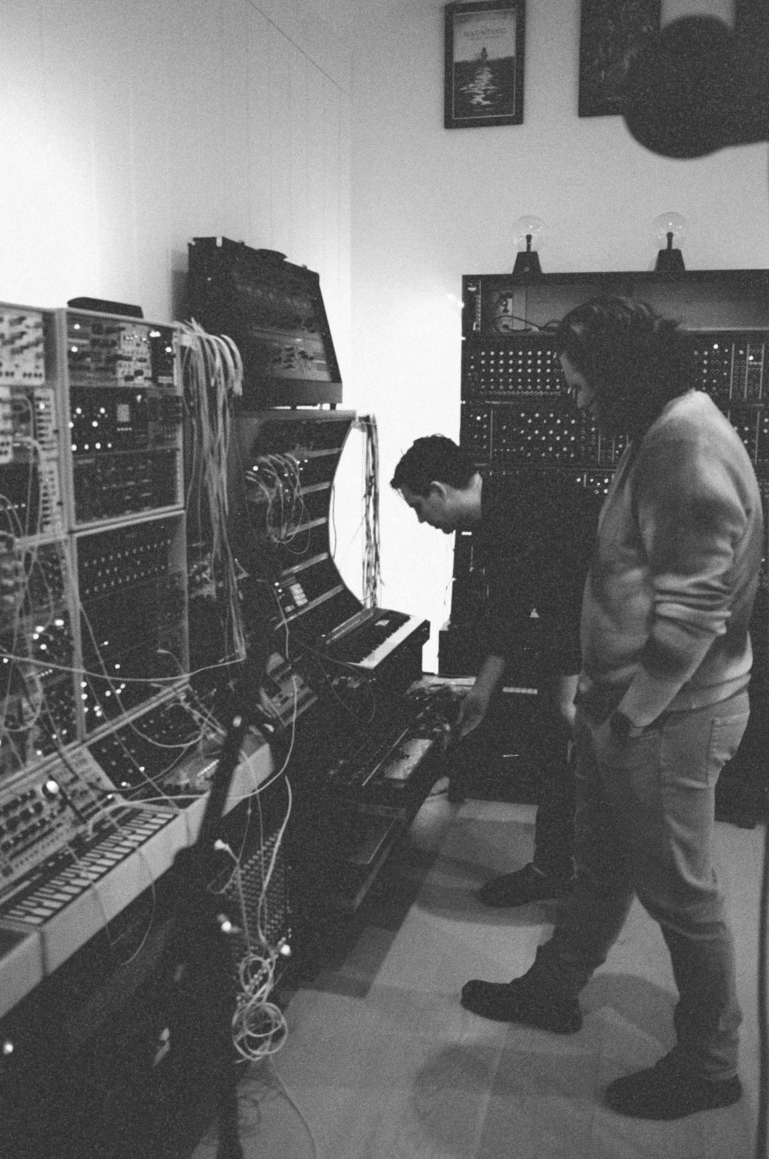 Two people working in a music studio filled with keyboards, synthesizers, and audio equipment.